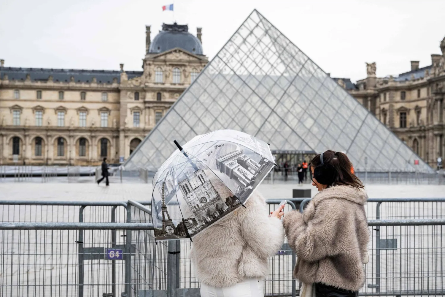 (FILES) Tourists stand next to barriers blocking the plaza with the Louvre Pyramid. (Photo by Martin LELIEVRE / AFP) 