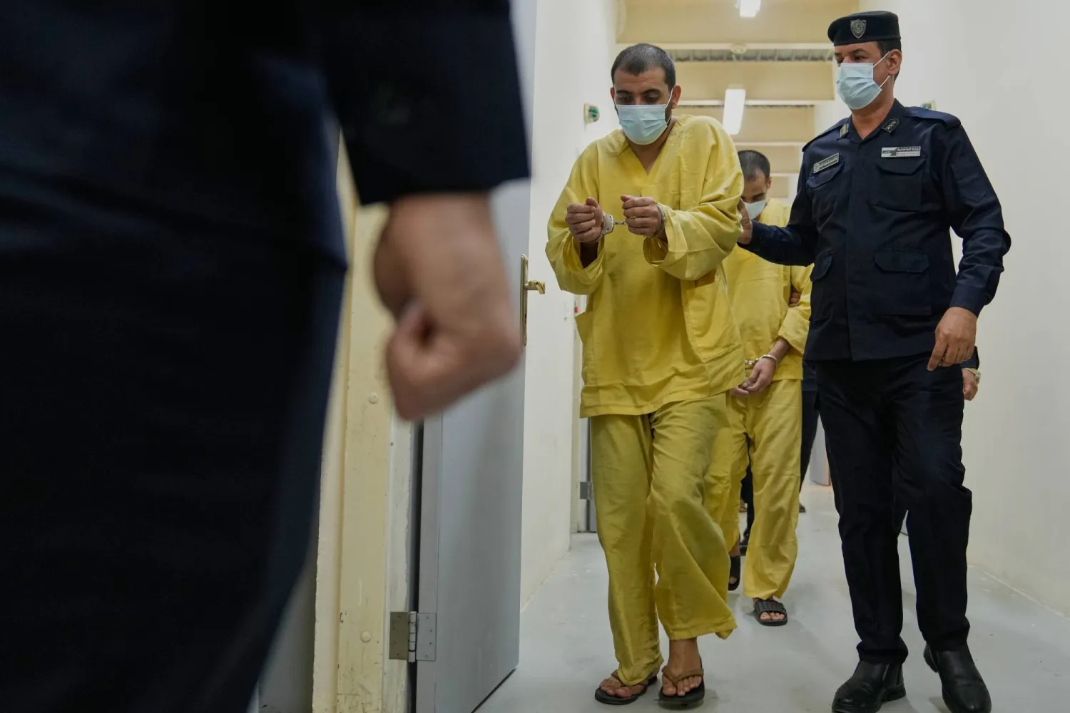 رجل أمن عراقي مع مشتبهين بالانتماء إلى «داعش» في سجن الكرخ ببغداد (أ.ب)