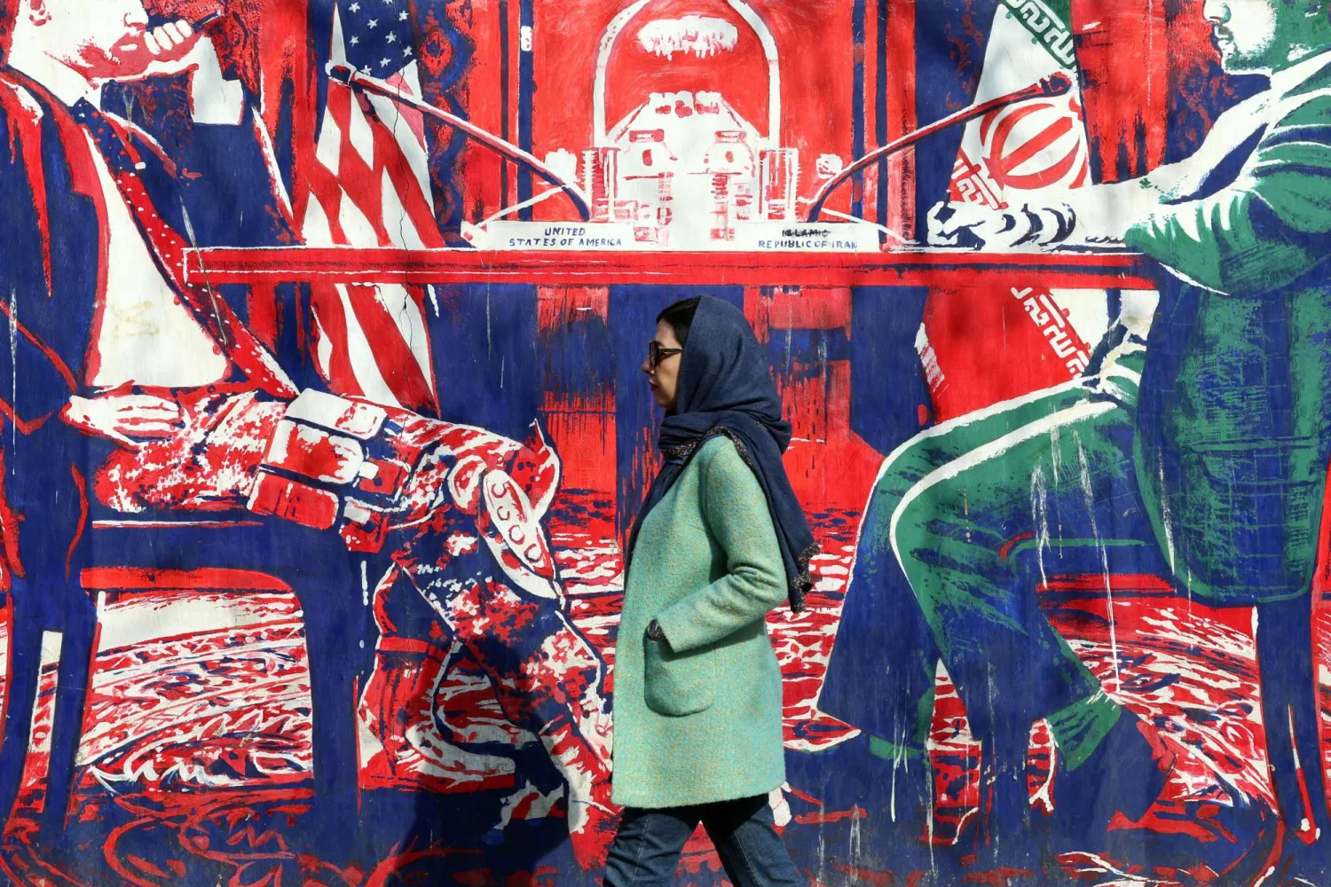 An Iranian woman walk past anti-US mural depicting Iran and US negotiation table, painted on the outer walls of the former US embassy, in Tehran on February 6, 2026. (AFP)