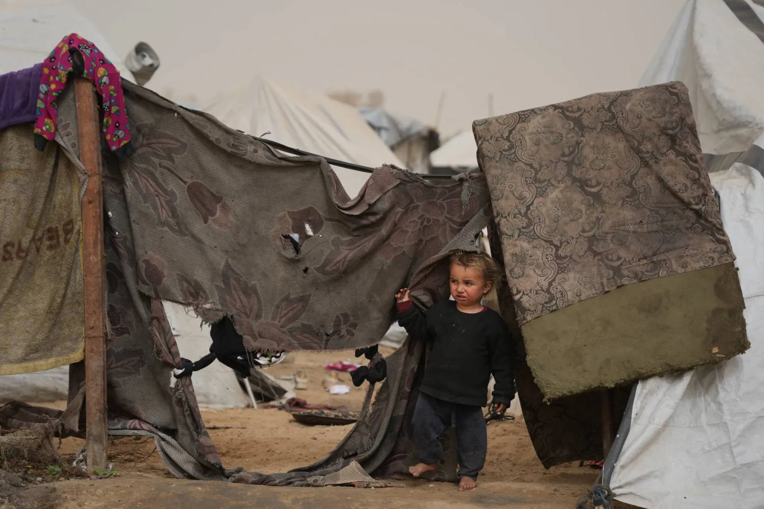 Palestinian child looks on as he stands next to a tent at a makeshift camp for displaced people during a dust storm in Zawaida, in the central Gaza Strip, Saturday, Feb. 14, 2026. (AP Photo/Abdel Kareem Hana)