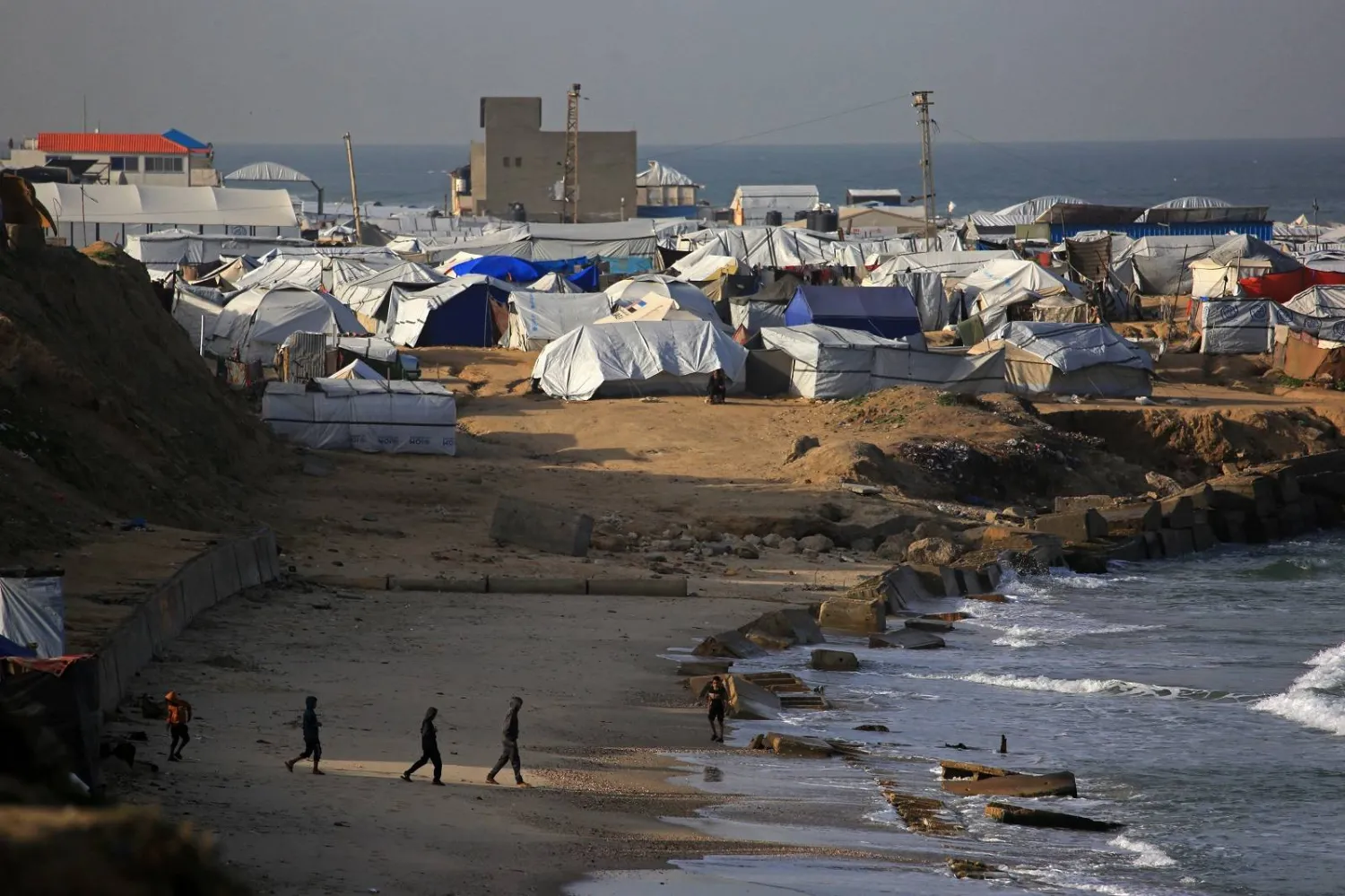 يسير الناس بالقرب من الخيام التي تؤوي الفلسطينيين النازحين في منطقة مواصي خان يونس جنوب قطاع غزة (أ.ف.ب)