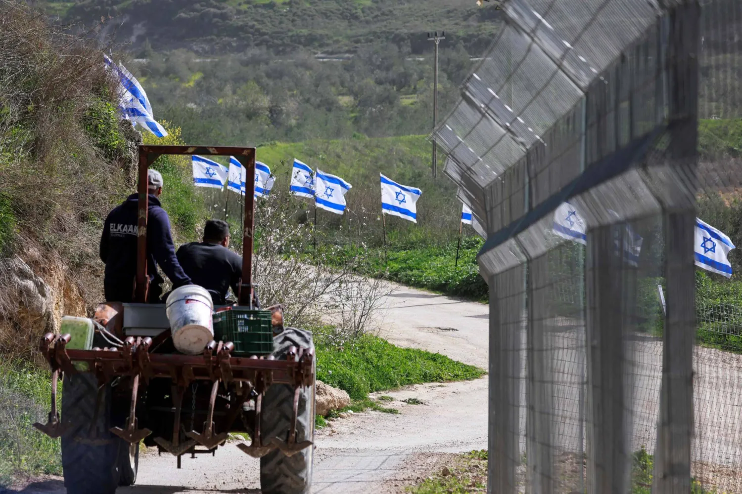 مزارعان فلسطينيان من قرية برقة في الضفة الغربية يستقلان جرارا بمحاذاة سياج نصبه مستوطنون أمس (أ.ف.ب)