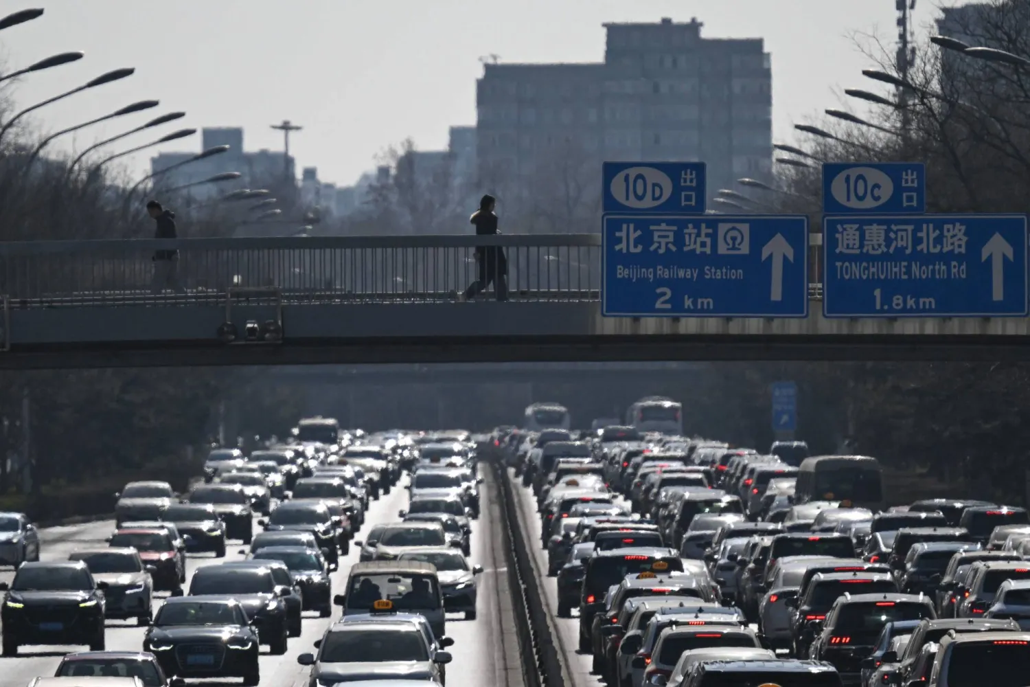 This picture taken on February 11, 2026 shows pedestrians walking along an overpass as traffic snarls in Beijing. (AFP)
