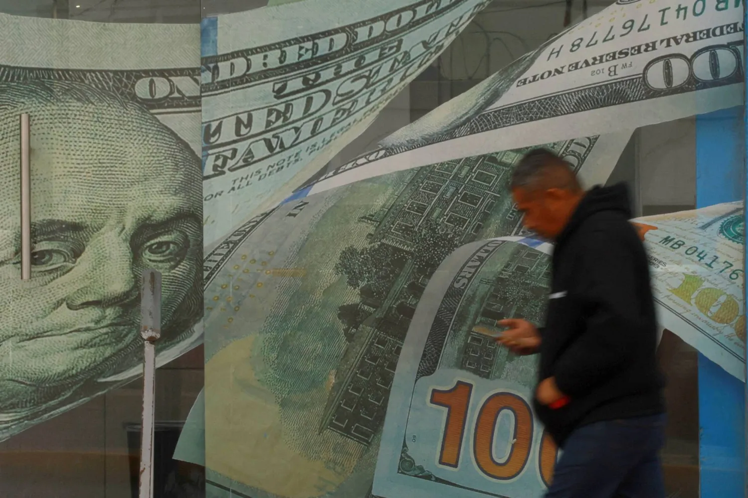 رجل يمر أمام محل صرافة مزين بلوحات من الفينيل عليها صور أوراق نقدية من فئة الدولار في سيوداد خواريز بالمكسيك (رويترز)