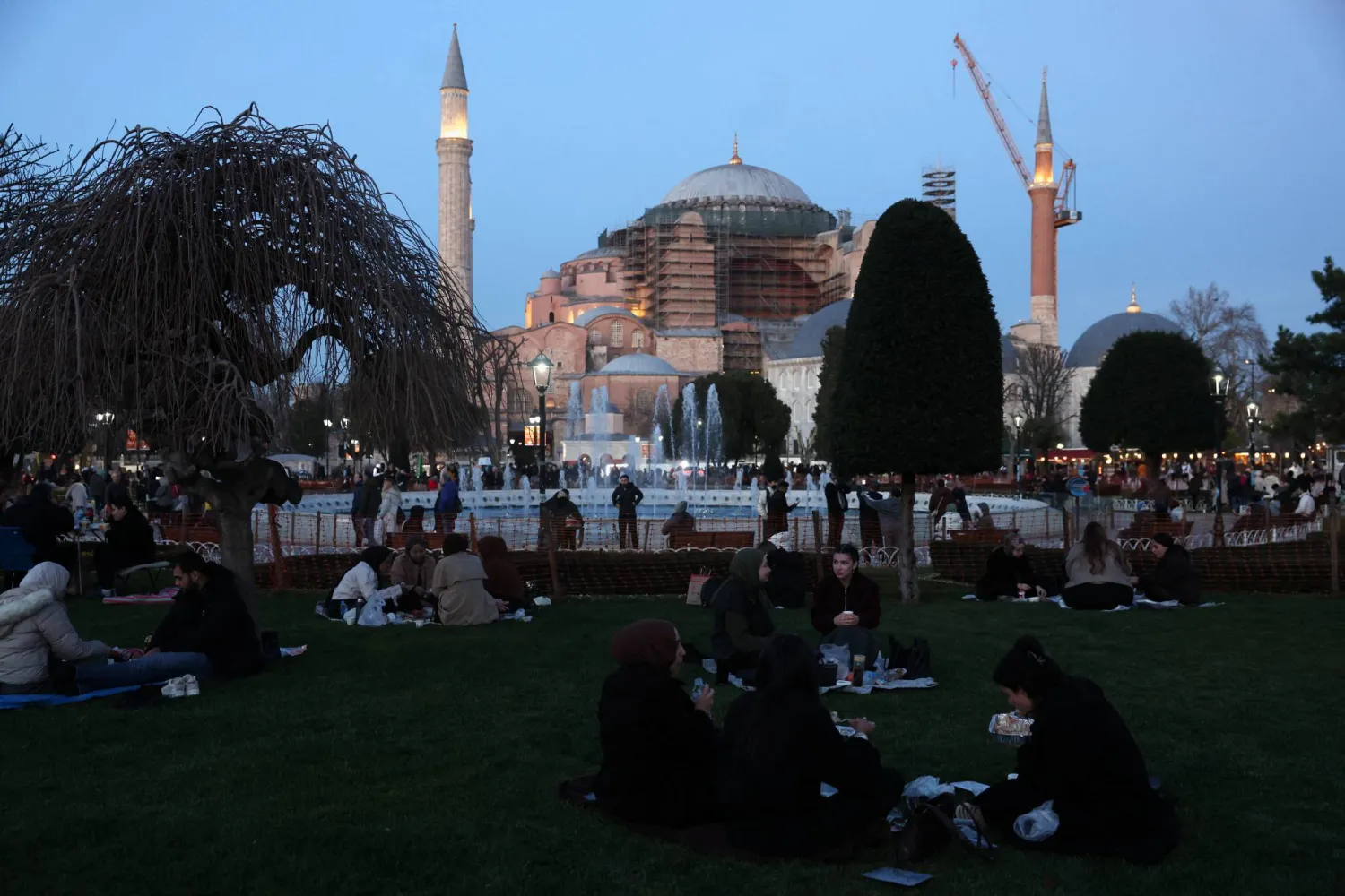 صائمون وقت الإفطار في ساحة مسجد السلطان أحمد بمدينة إسطنبول التركية ويبدو في الخلفية مسجد أيا صوفيا (رويترز)