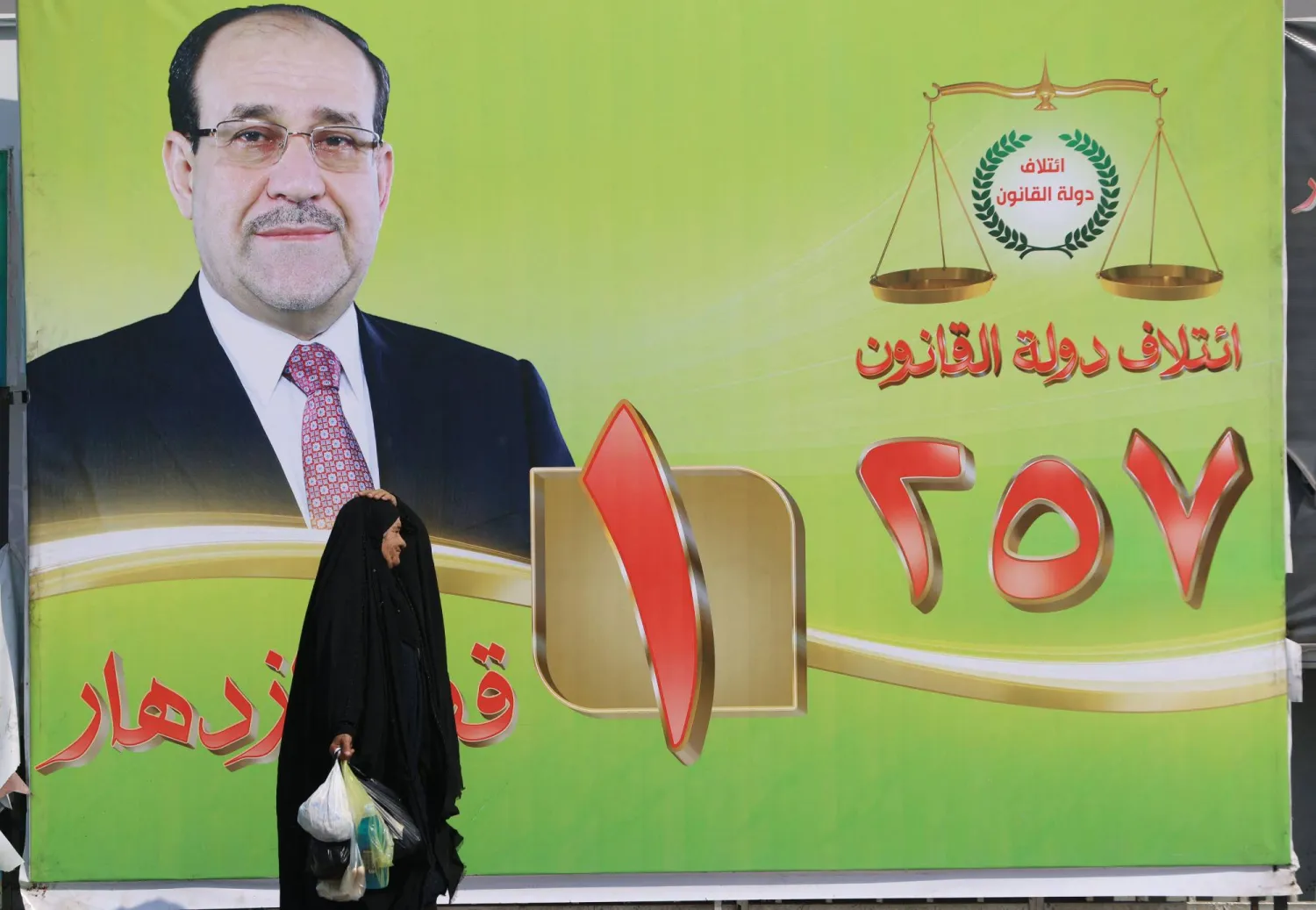امرأة تمر أمام لوحة إعلانية انتخابية تحمل صورة رئيس الوزراء العراقي السابق نوري المالكي في وسط بغداد يوم 19 أكتوبر 2025 (أ.ف.ب)