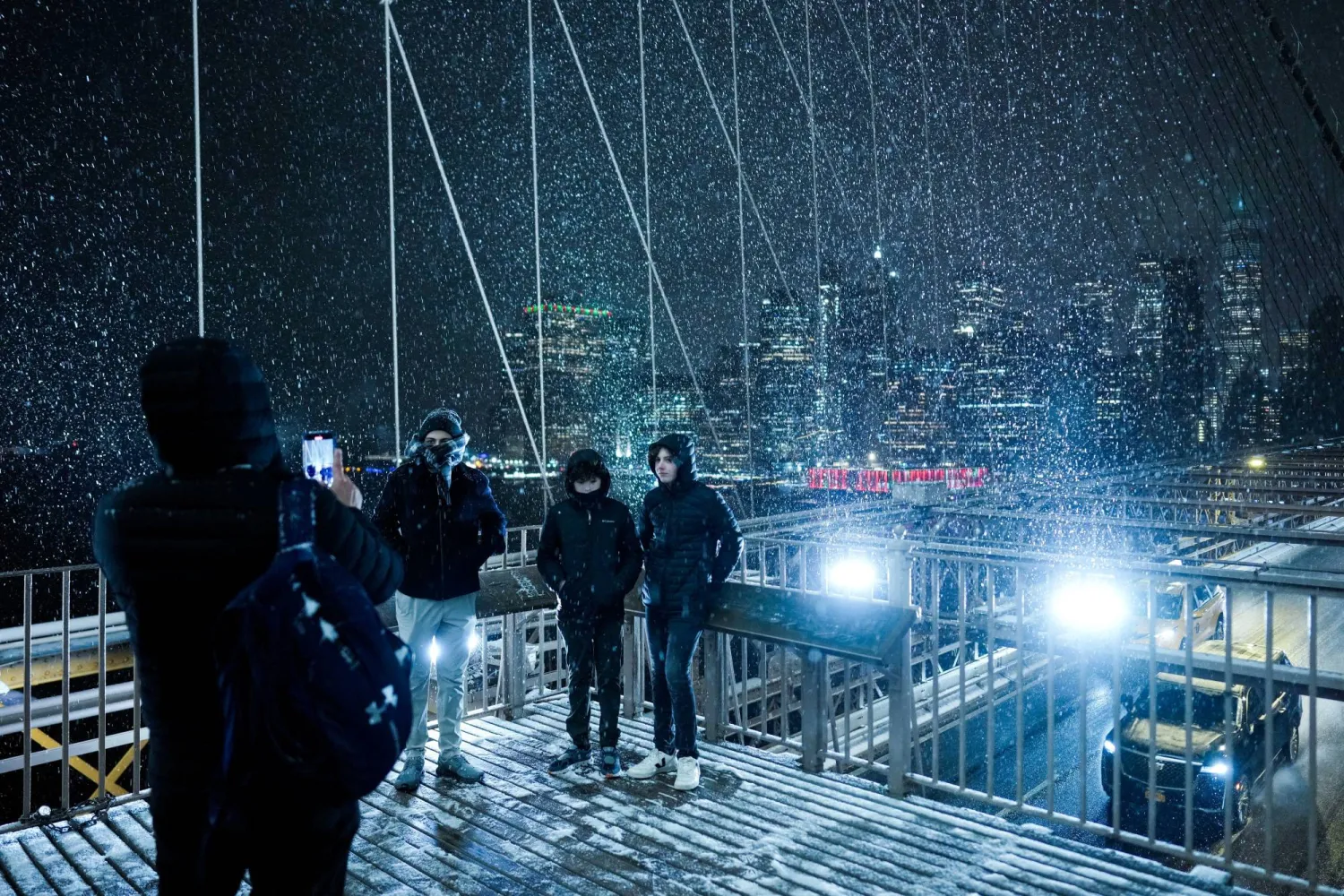 أشخاص يلتقطون الصور على جسر بروكلين أثناء تساقط الثلوج خلال عاصفة شتوية في مدينة نيويورك (رويترز)