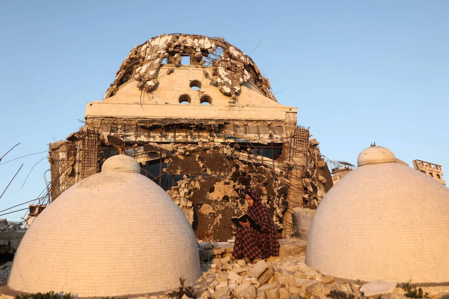 A female member of the al-Ghafir family, sits of the debris of the al-Hasayna Mosque as she recites from a copy of the Quran, during the holy month of Ramadan in western Gaza City on February 21, 2026. (Photo by Omar AL-QATTAA / AFP)