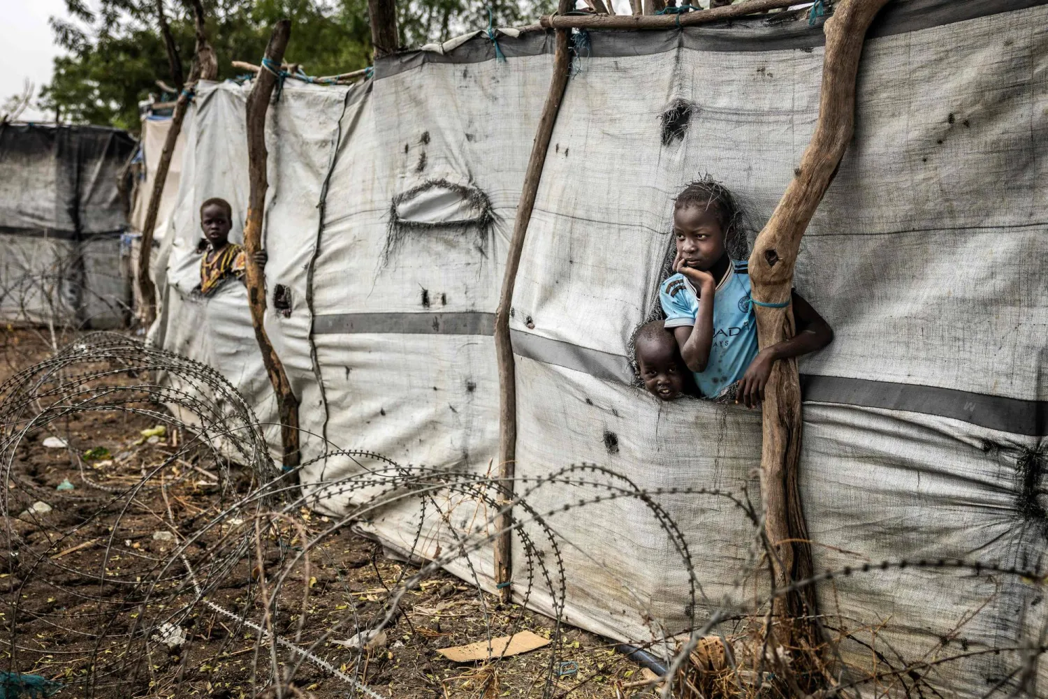 Children poke their heads and arms through holes in makeshift fabric fences in the strategic opposition-controlled town of Akobo, Jonglei State, on February 12, 2026. (AFP)