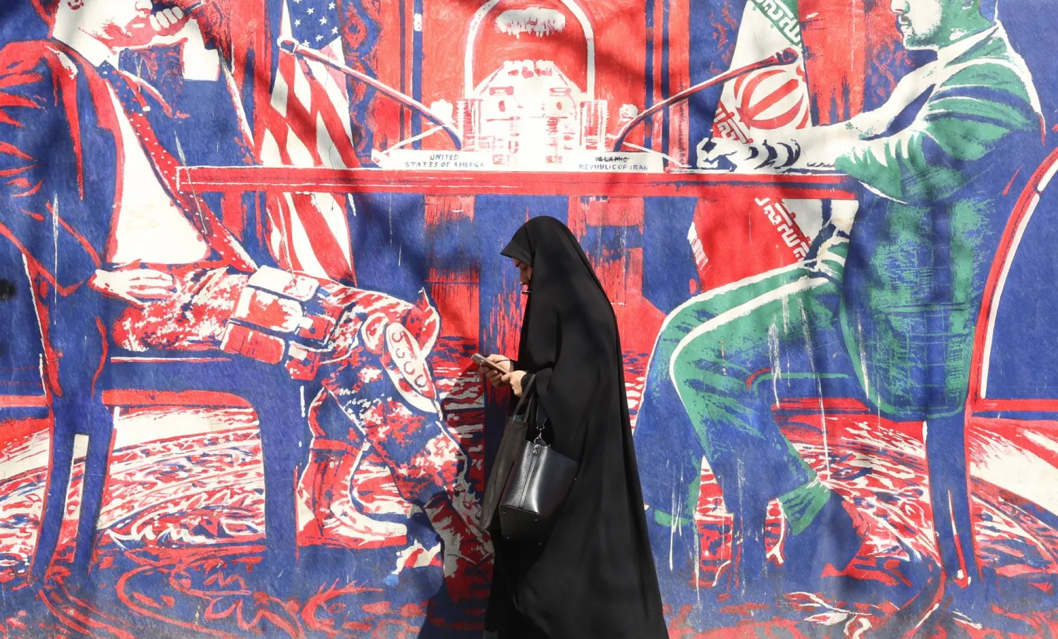 A veiled Iranian woman walks past an anti-US mural in Tehran, Iran, 23 February 2026. (EPA)