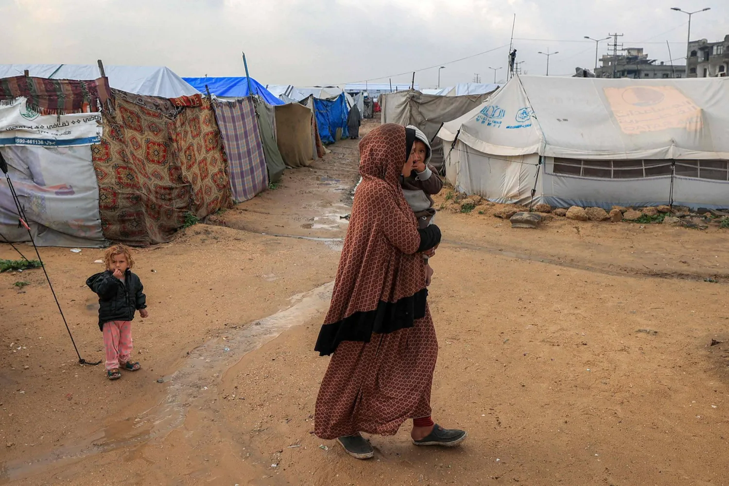 نازحة فلسطينية تسير حاملة طفلها على أرض بللتها مياه الأمطار بمخيم البريج للاجئين بوسط قطاع غزة يوم الثلاثاء (أ.ف.ب)