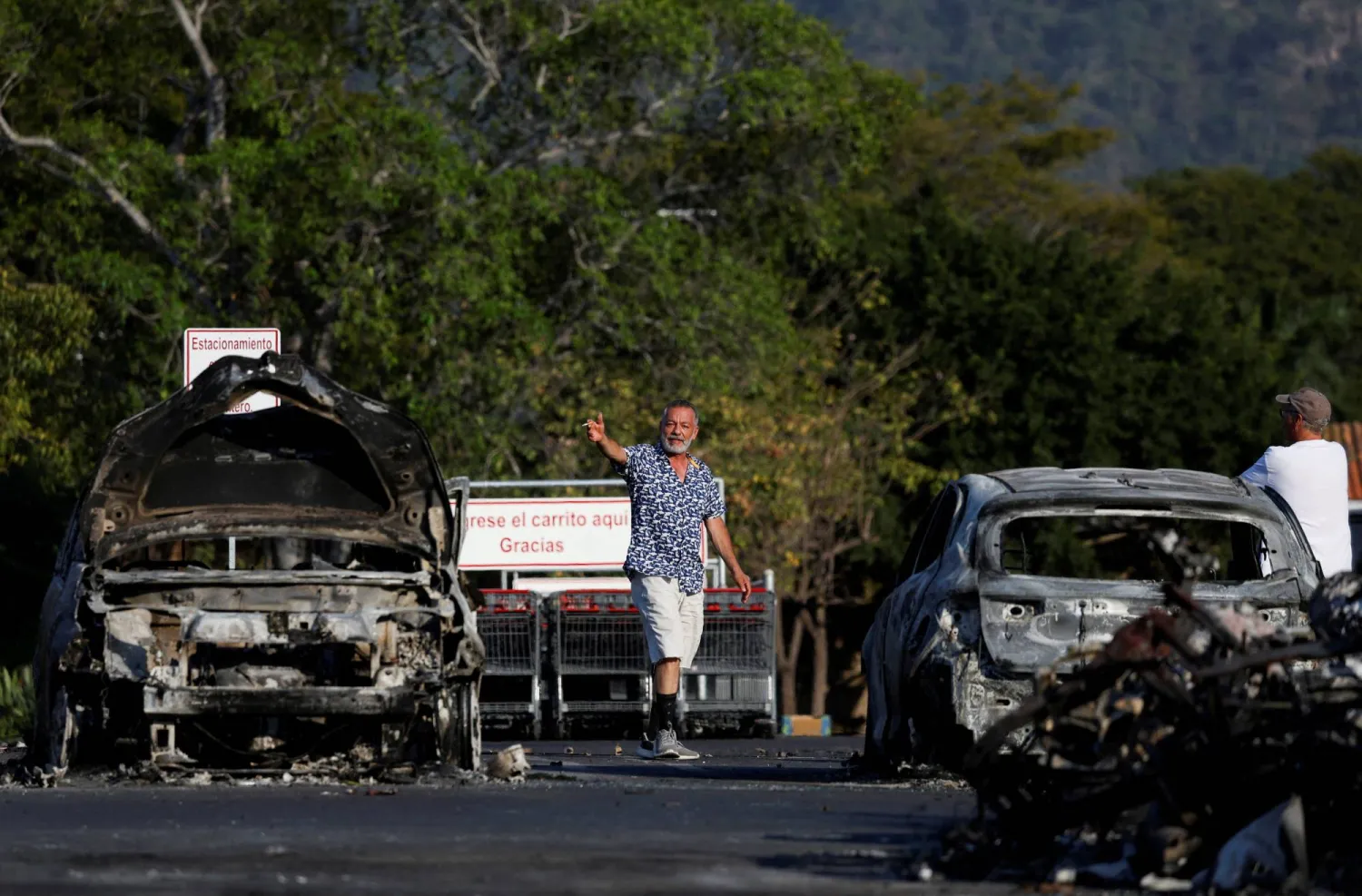 People walk at a parking lot of a supermarket where several vehicles were consumed by flames days after a series of blockades and attacks by organized crime following a military operation in which drug cartel leader Nemesio Oseguera, known as "El Mencho," was killed, in Puerto Vallarta, Mexico, February 24, 2026. REUTERS/Daniel Becerril