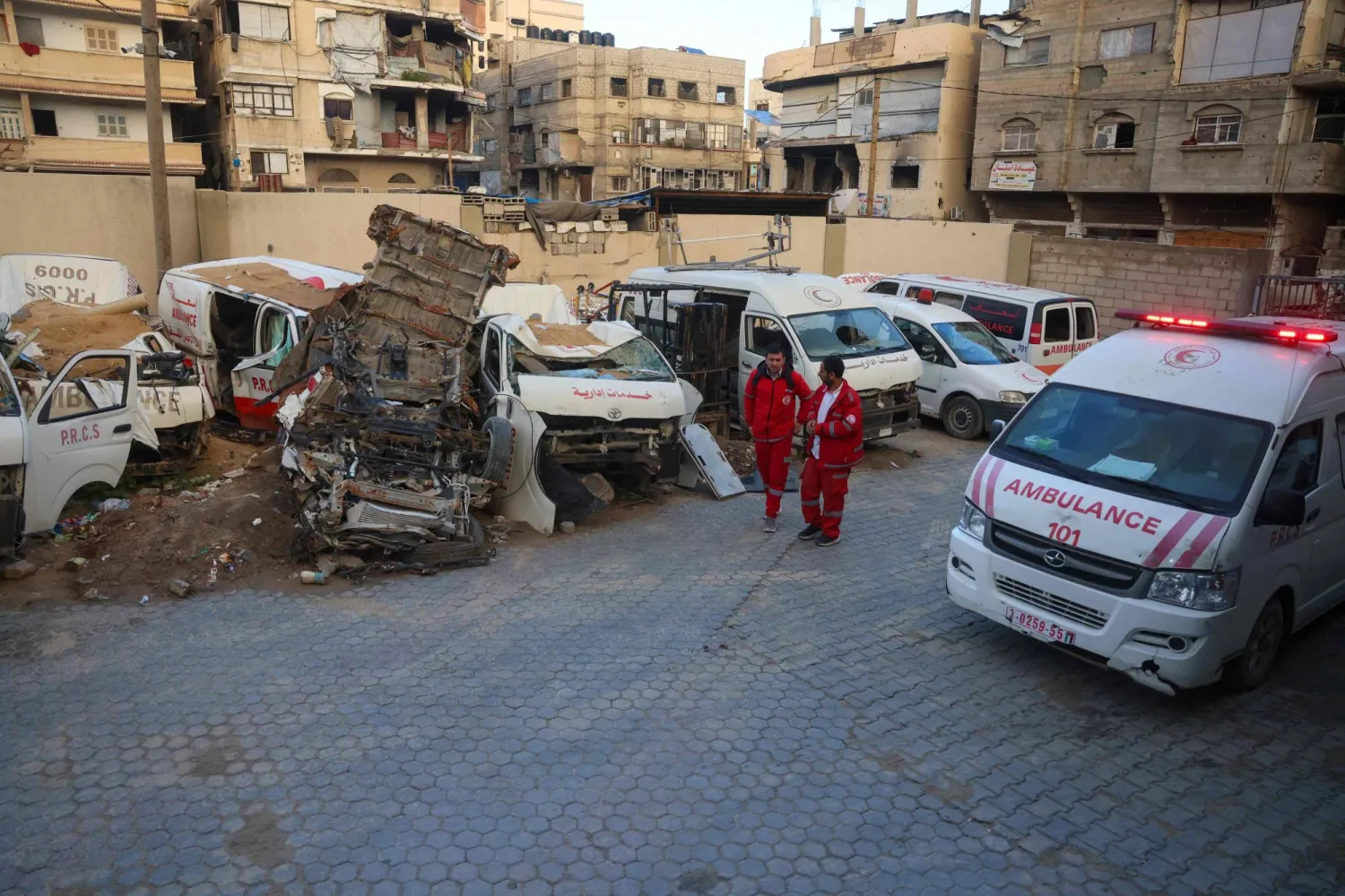 يسير مسعفون فلسطينيون أمام سيارات إسعاف مدمرة في مقر جمعية الهلال الأحمر الفلسطيني في خان يونس جنوب قطاع غزة (أ.ف.ب)