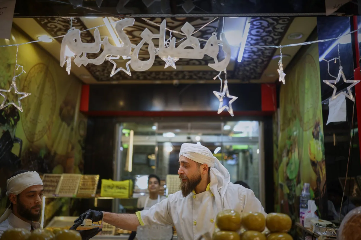 بائع متجول يعتني بكشكه المضاء جيداً والمليء بحلويات رمضان في دمشق (أ.ب)