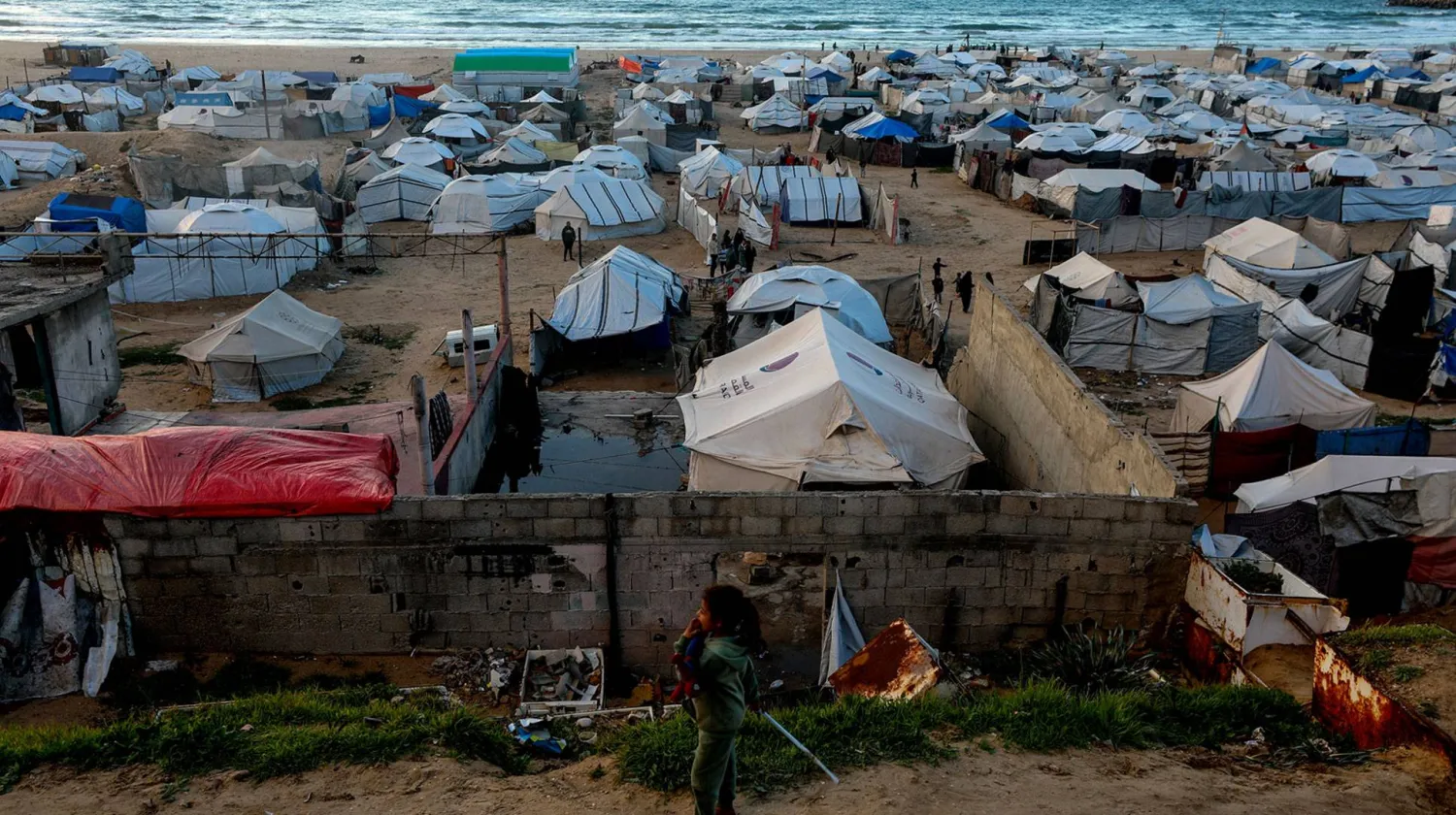 طفلة فلسطينية نازحة وخلفها خيام مؤقتة قرب شاطئ مدينة غزة (إ.ب.أ)