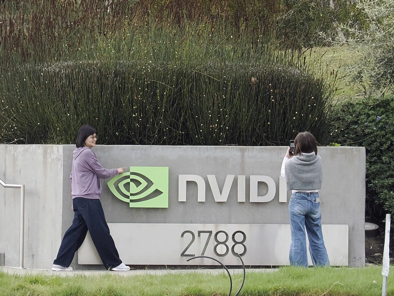 شخصان يلتقطان صوراً لشعار شركة «إنفيديا» خارج مقرها الرئيسي في سانتا كلارا بكاليفورنيا (إ.ب.أ)