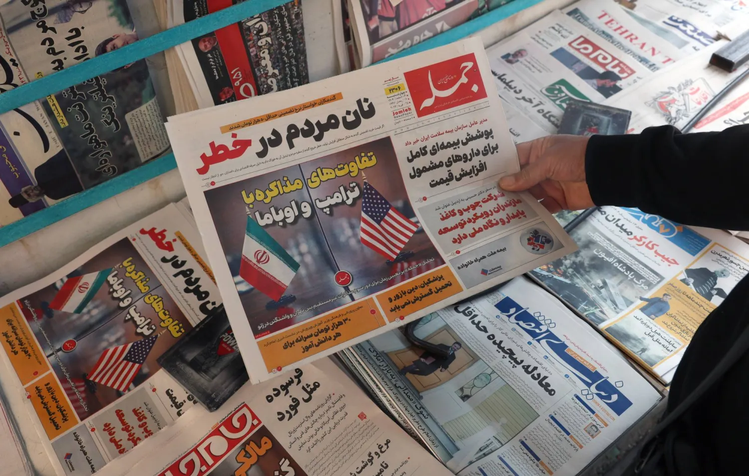 رجل إيراني يحمل نسخة من صحيفة «جومله» الإيرانية اليومية تحمل عنواناً باللغة الفارسية: «الاختلافات بين التفاوض مع دونالد ترمب وباراك أوباما» (إ.ب.أ)