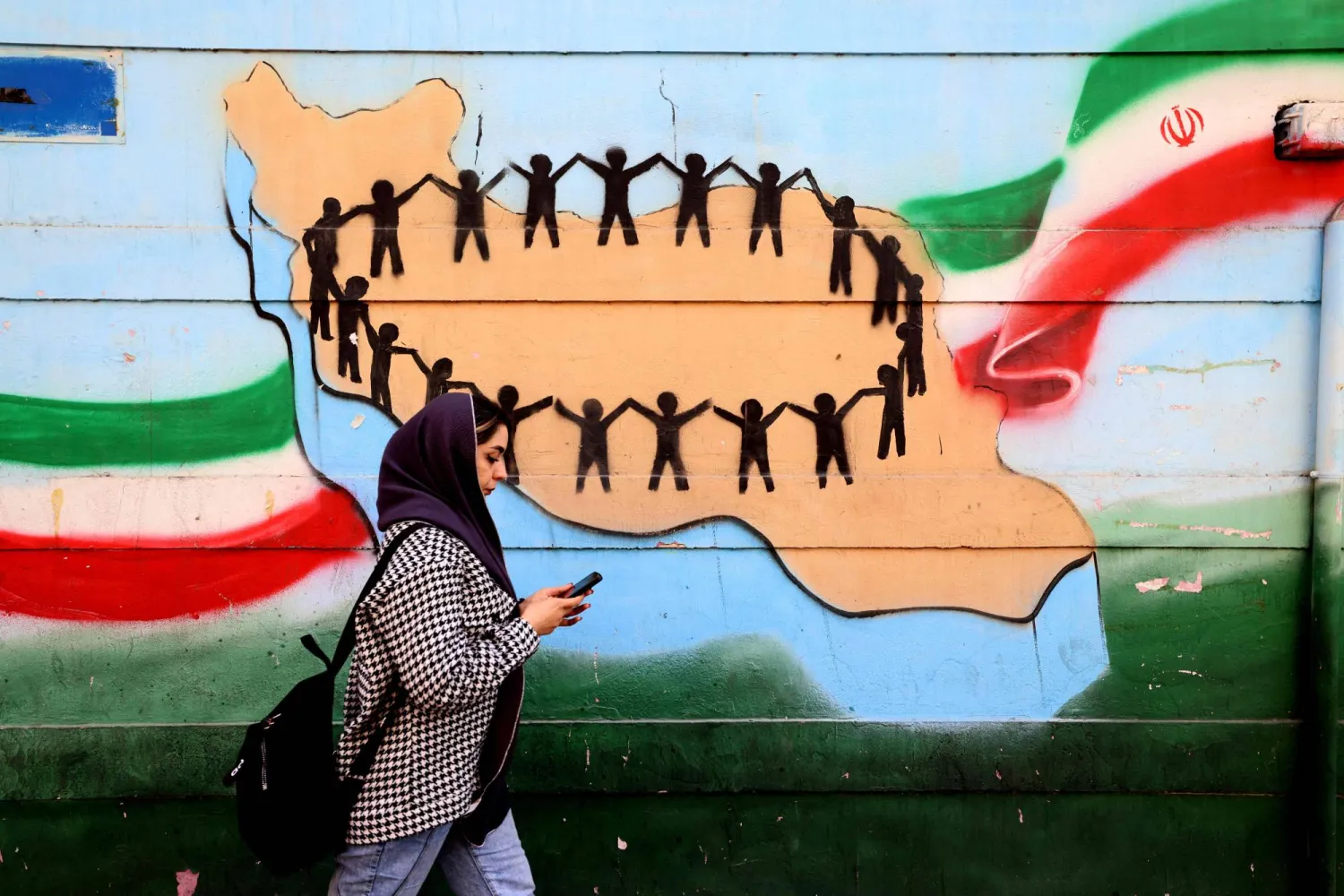 A woman walks past the flag and map of Iran painted on a wall in Tehran on February 25, 2026. (Photo by ATTA KENARE / AFP)