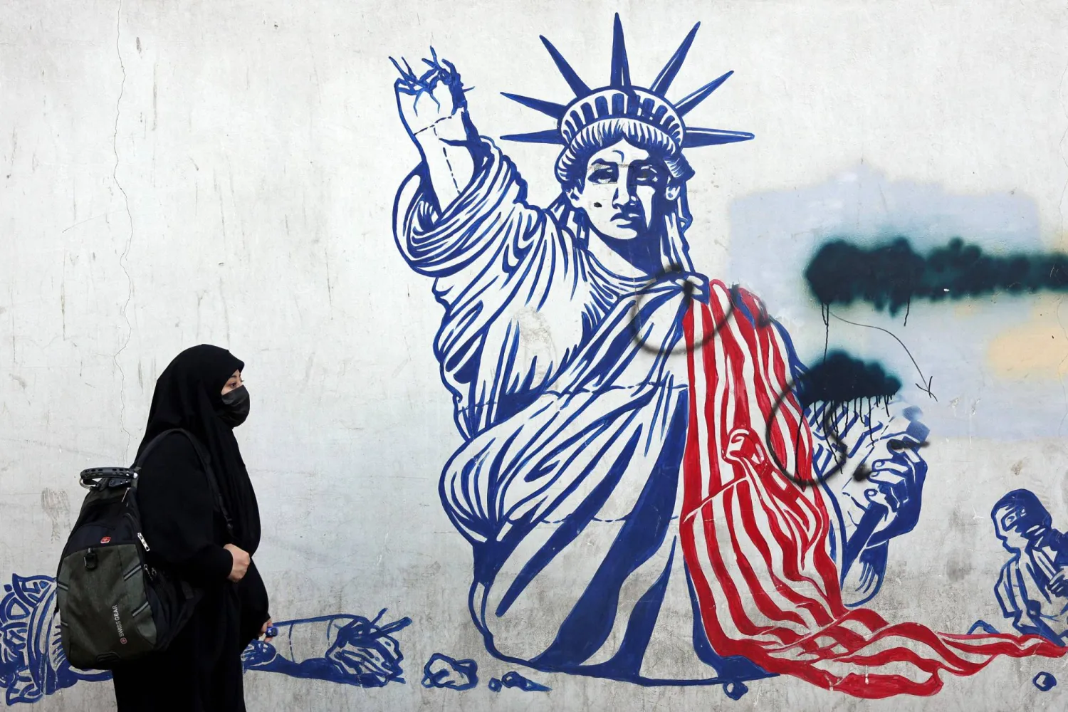 A veiled Iranian woman walks past an anti-US mural next to former US embassy in Tehran on February 26, 2026. (AFP)