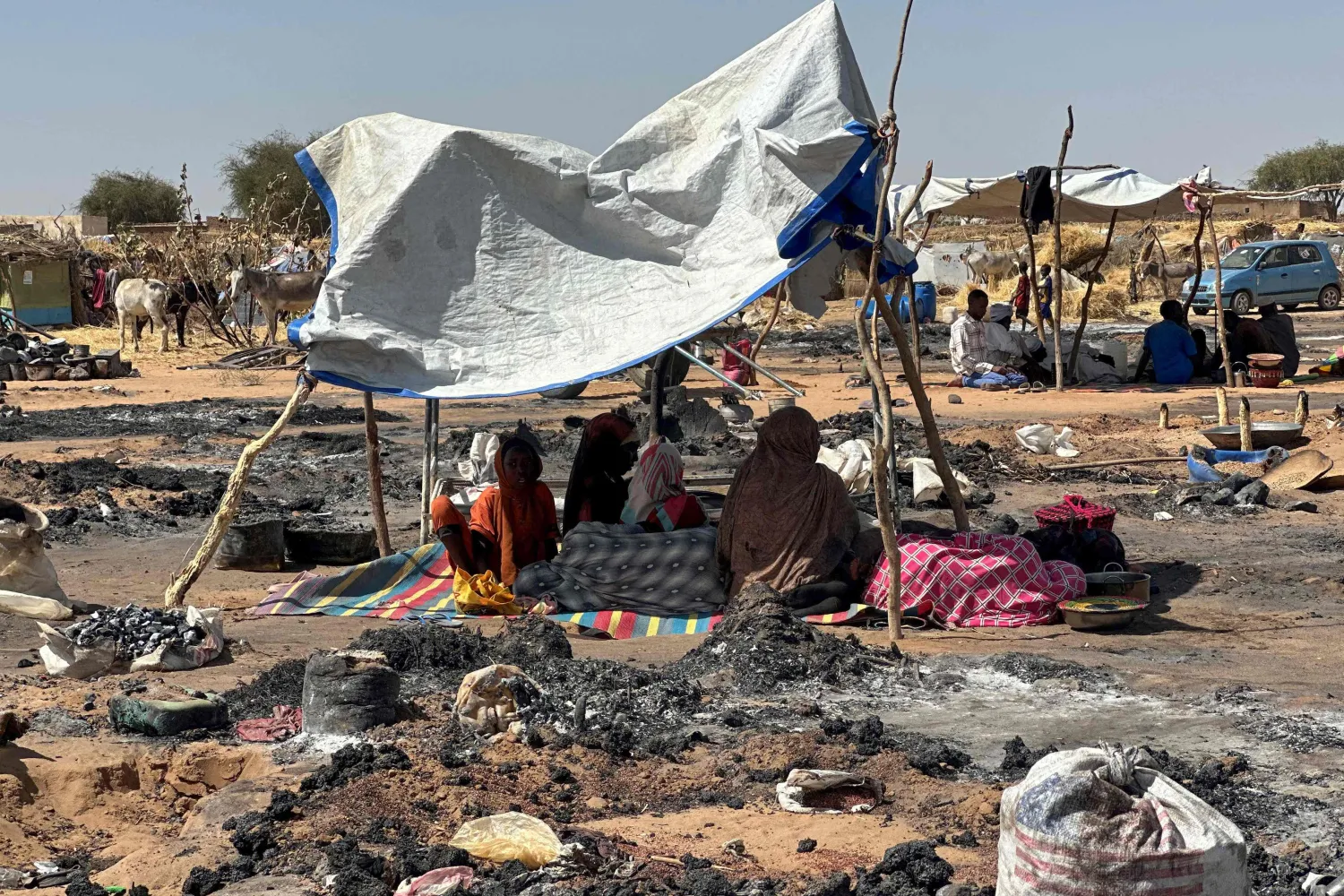Displaced Sudanese people who left el-Fasher after its fall, sit in the shade in Tawila amid the remains of a fire that broke out in the camp on February 11, 2026. (AFP) 