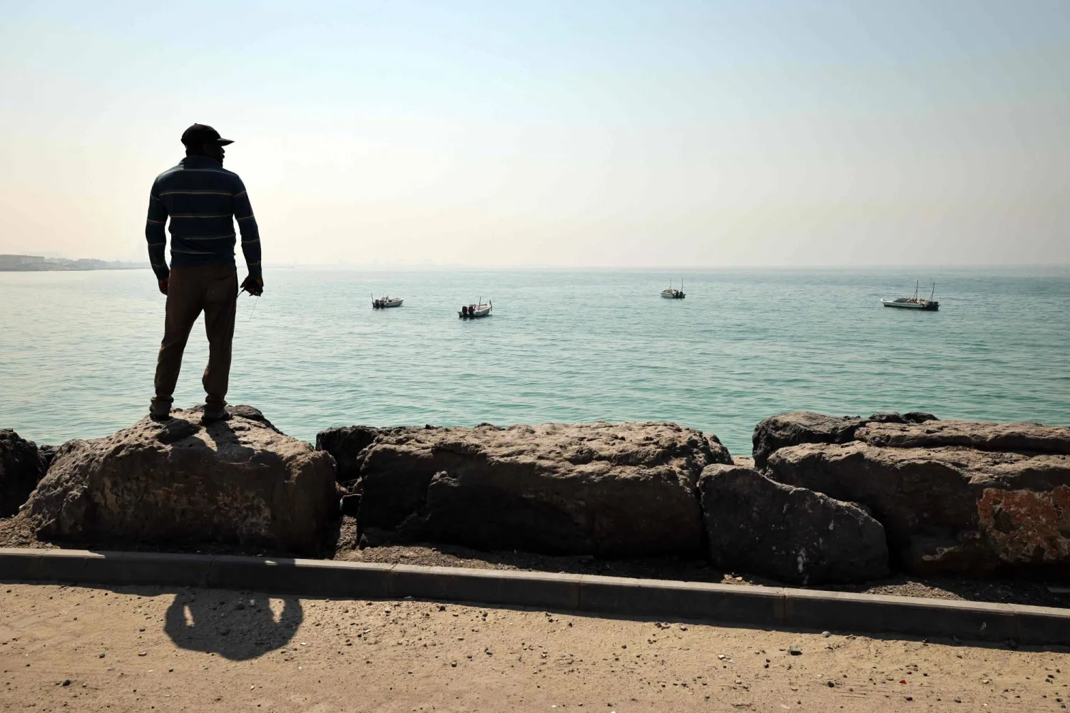 صياد ينظر نحو الأفق بميناء الصيد في العقير على مضيق هرمز بإمارة رأس الخيمة الشمالية (أ.ف.ب)