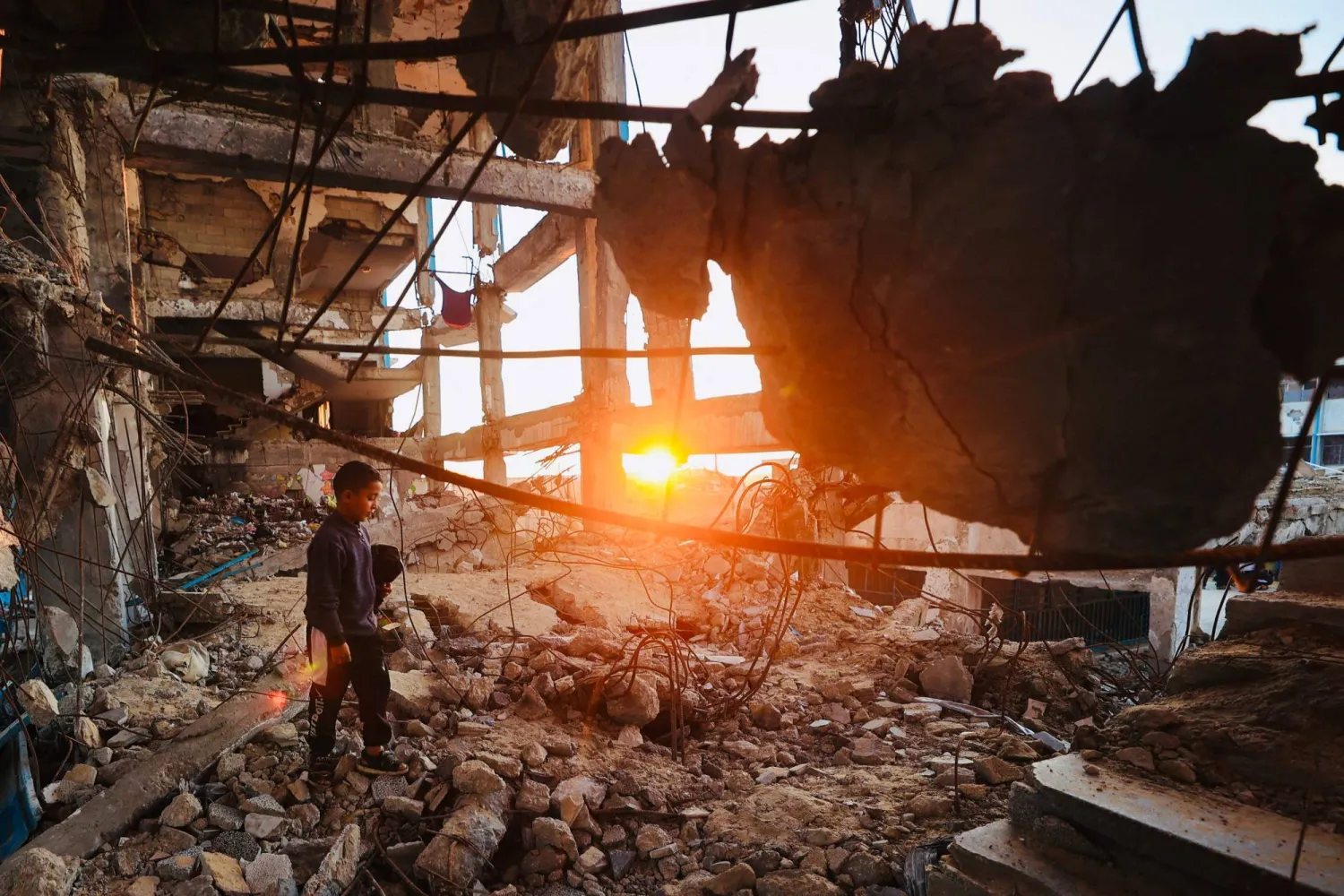 A displaced Palestinian boy walks over the rubble before taking the "iftar" fast-breaking meal during the Muslim holy month of Ramadan, amidst the destruction in Bureij refugee camp in the central Gaza Strip on February 25, 2026. (Photo by Eyad Baba / AFP)