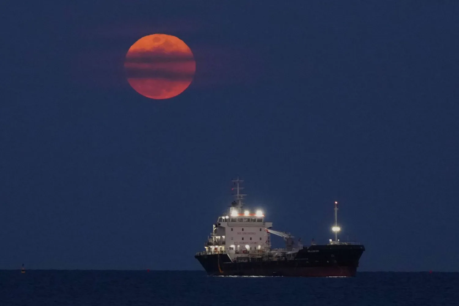 A blood moon rises over the Mediterranean sea where a ship is anchored, in Limassol, Cyprus, Tuesday, March 3, 2026. (AP Photo/Petros Karadjias)
