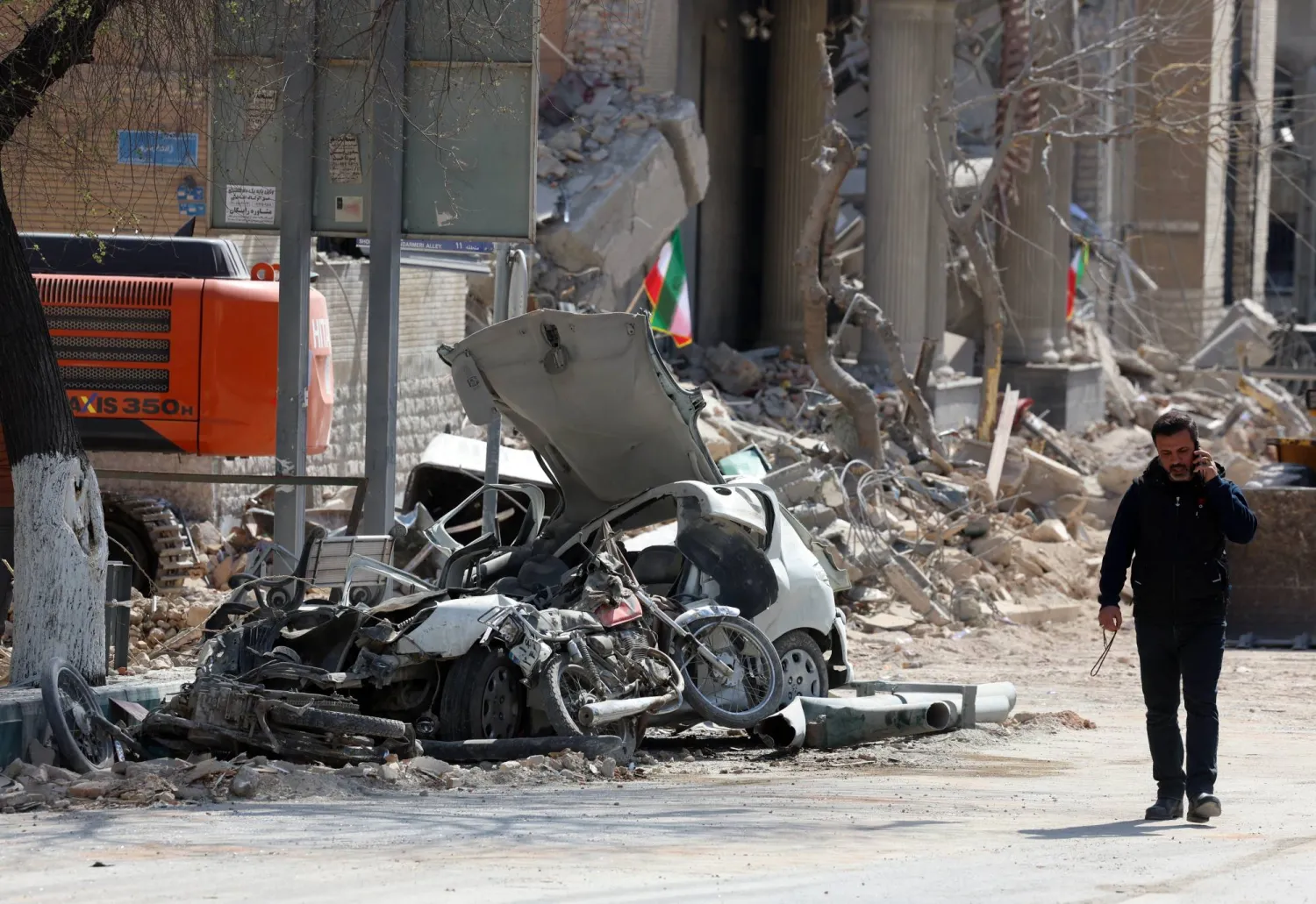 رجل إيراني يسير بجوار الأنقاض والسيارات المحطمة بوسط طهران (إ.ب.أ)