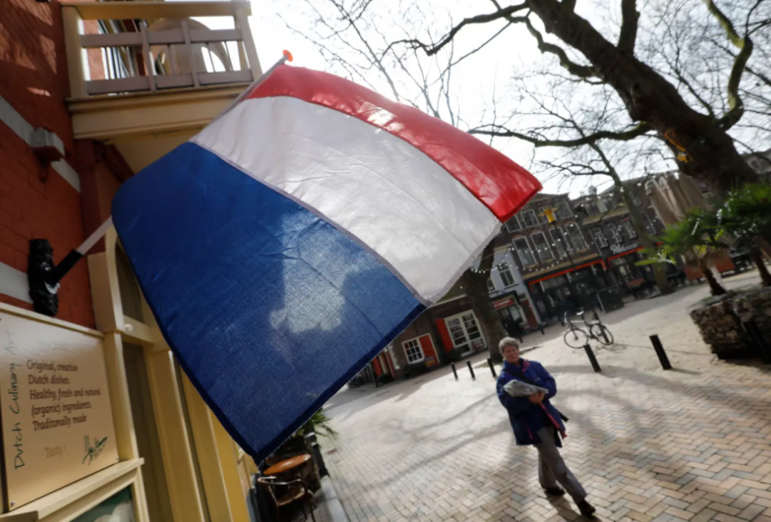 A woman walks past a national flag, the day before a general election, in Delft, Netherlands, March 14, 2017. REUTERS/Yves Herman 