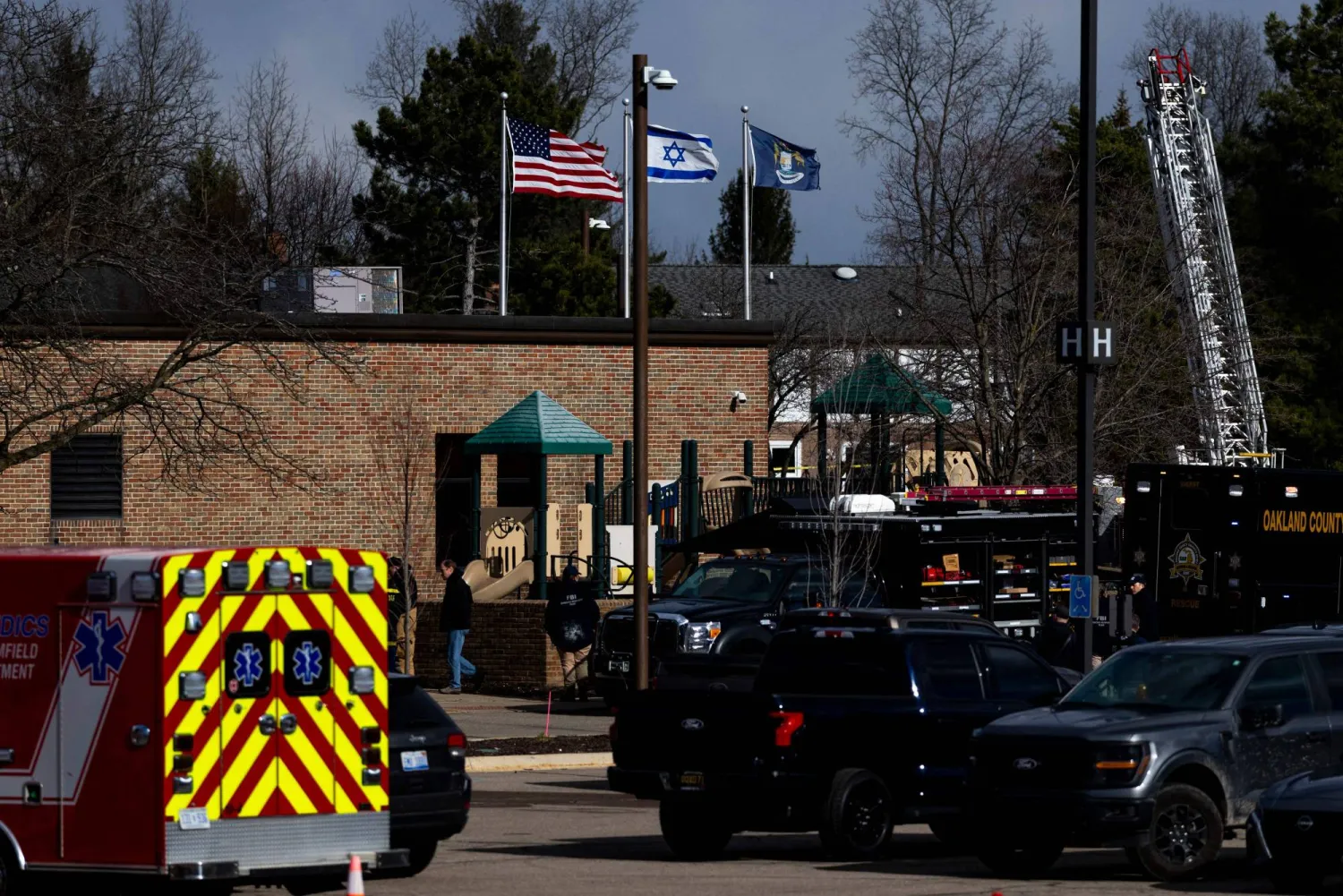 WEST BLOOMFIELD, MICHIGAN - MARCH 12: Law enforcement vehicles in the parking lot of Temple Israel as an Israeli flag blows in the wind on top of the building following an active shooter on March 12, 2026 in West Bloomfield, Michigan. Emily Elconin/Getty Images/AFP ( 
