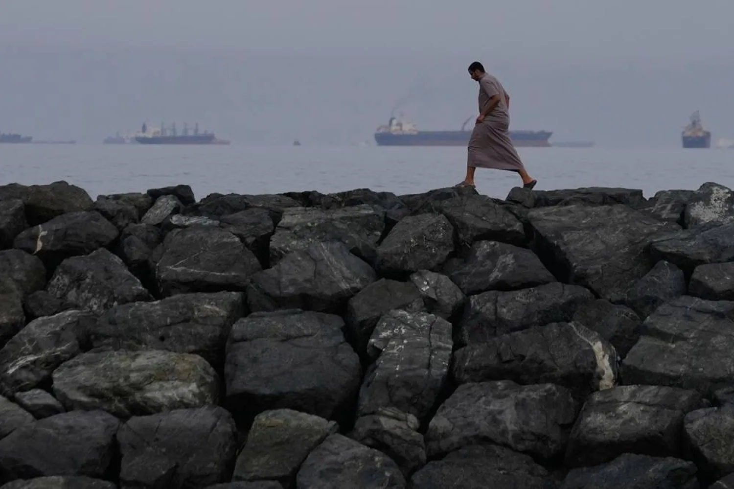 A man walks along the shore as oil tankers and cargo ships line up in the Strait of Hormuz, seen from Khor Fakkan, United Arab Emirates, Wednesday, March 11, 2026. (AP)