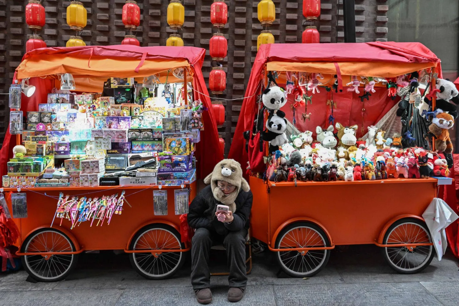 بائعة تتصفح هاتفها بينما تنتظر الزبائن في أحد شوارع العاصمة الصينية بكين (أ.ف.ب)