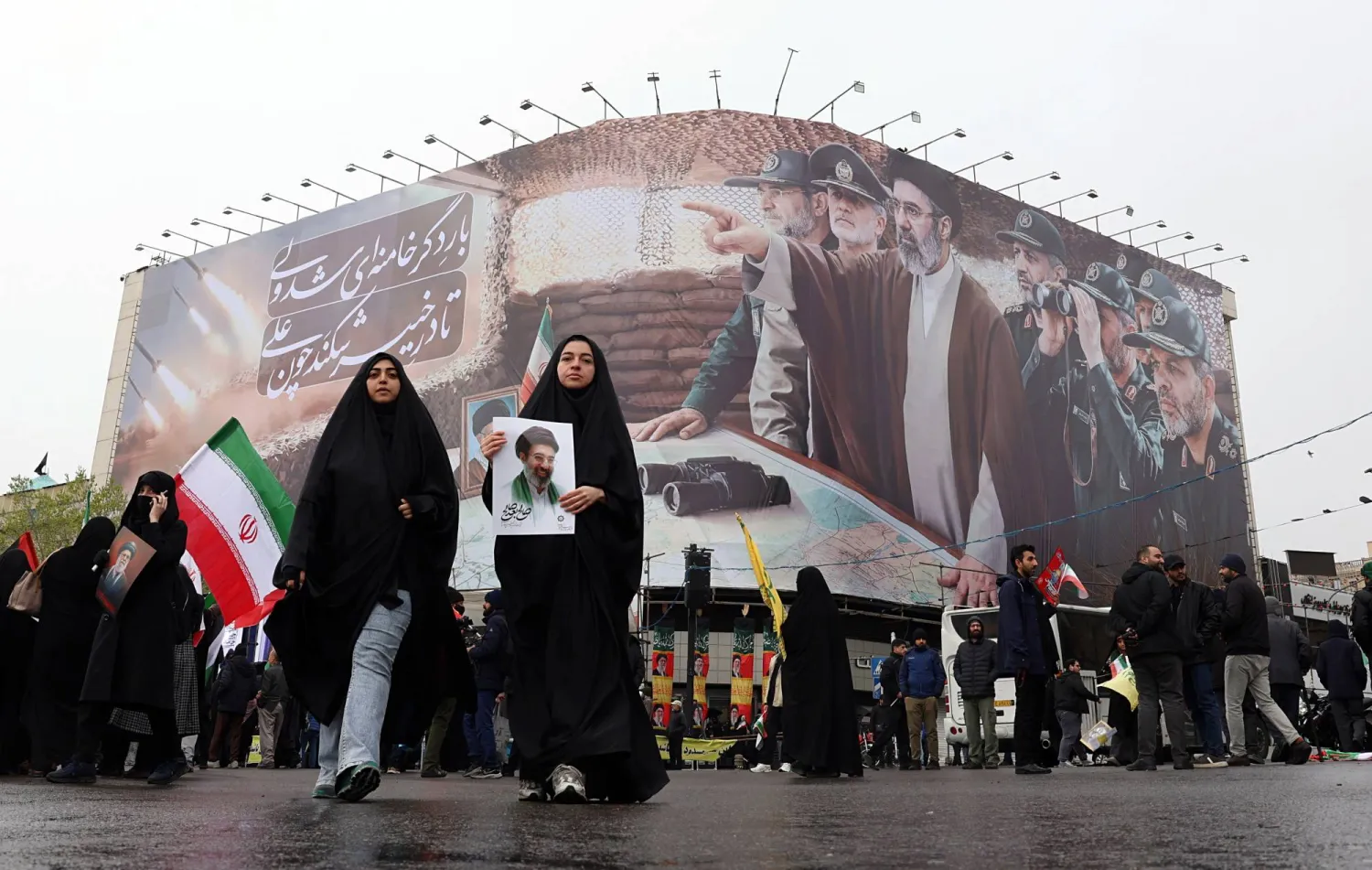 نساء إيرانيات يمشين أمام لوحة تحمل صور المرشد مجتبى خامنئي وقادة عسكريين خلال مسيرة في طهران (إ.ب.أ)