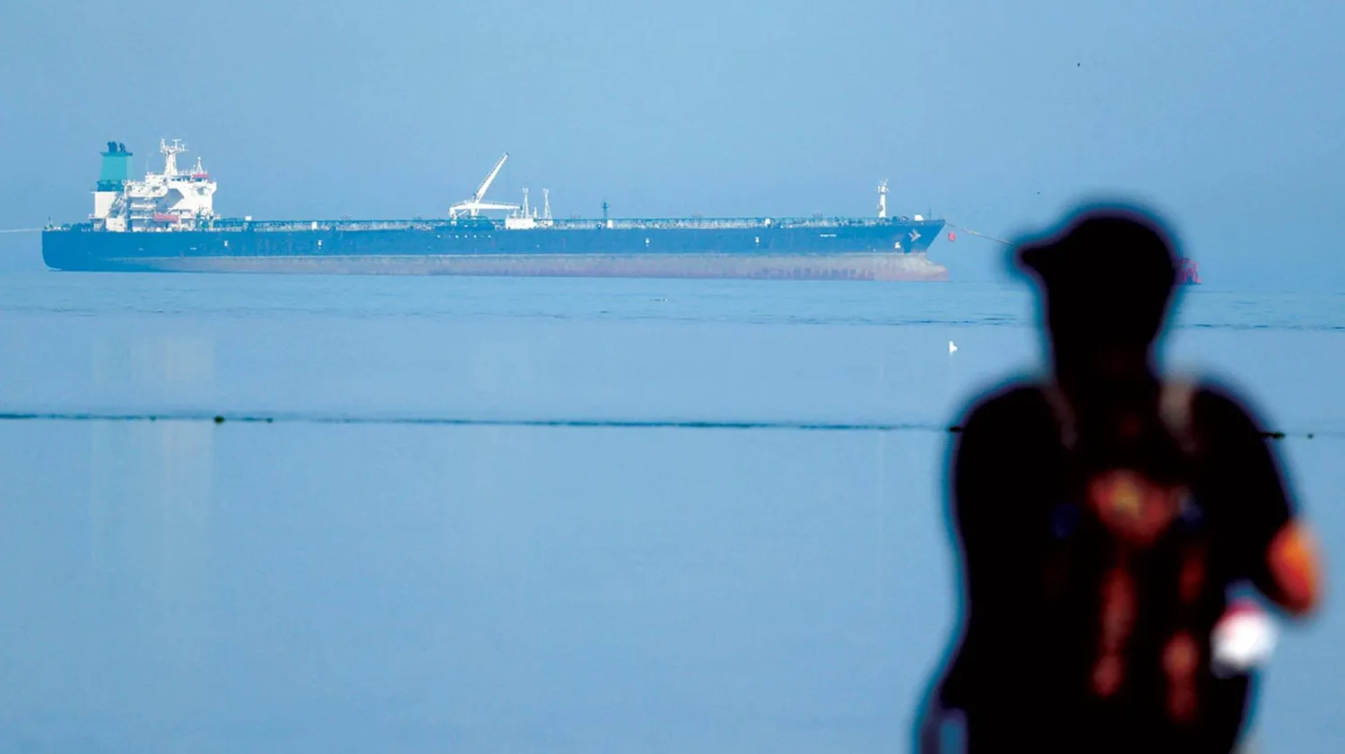 رجل يتابع ناقلة نفط روسية لدى مرورها قرب شاطئ ولاية غوجارات بالهند (رويترز)