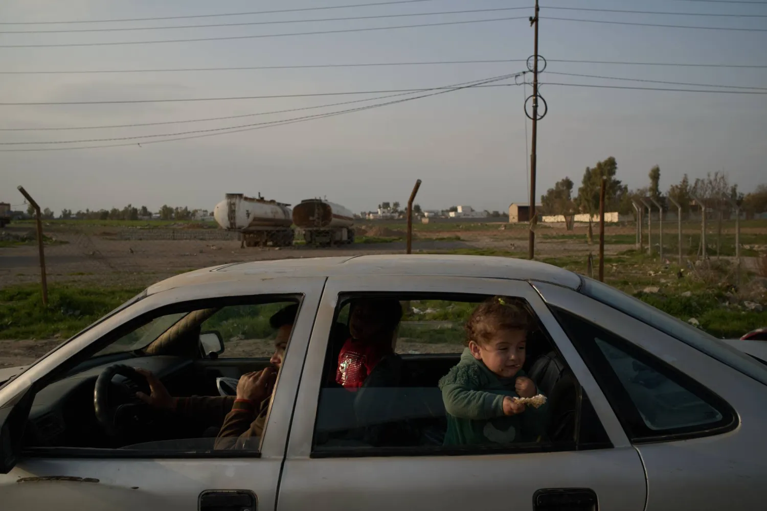 رجل برفقة أطفاله على طريق يمر بجانب شاحنات في ضواحي أربيل شمال العراق (أ.ب)