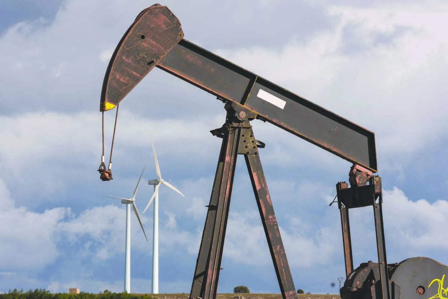 An oil pump is pictured at an obsolete oilfield, with wind turbines in the background, in Sargentes de la Lora on March 13, 2026, near Burgos in northern Spain, where oil first flowed in Spain in 1964.  (Photo by CESAR MANSO / AFP)