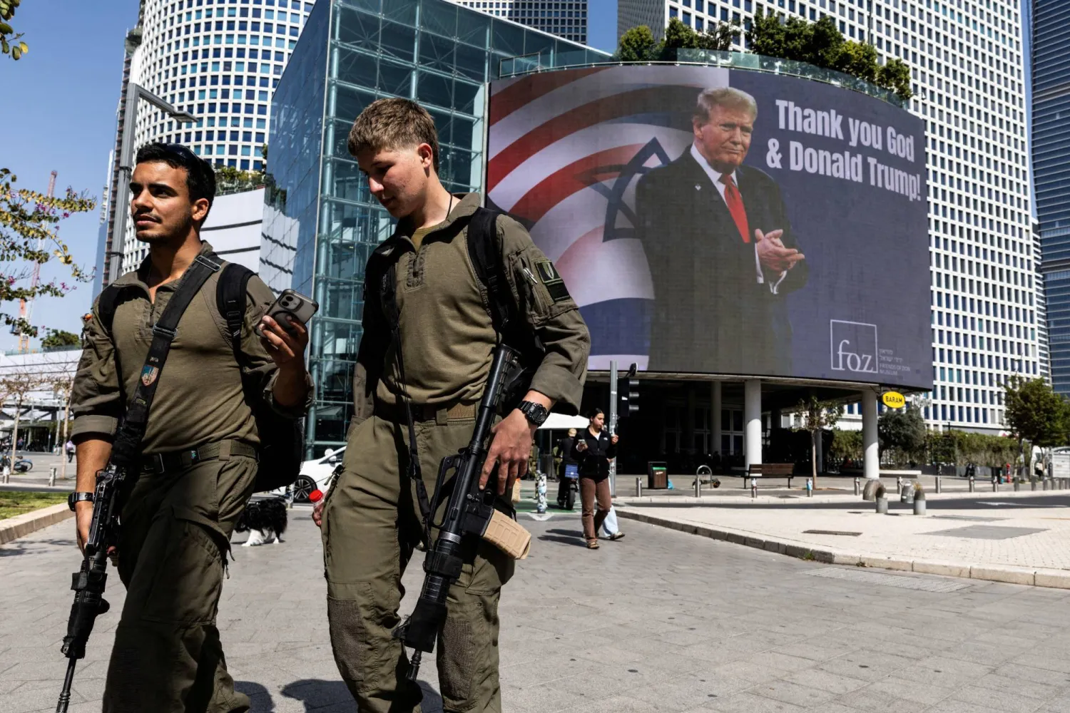 Two Israeli soldiers walk past a large billboard in central Tel Aviv reading “Thank you God and Donald Trump” (Reuters). 