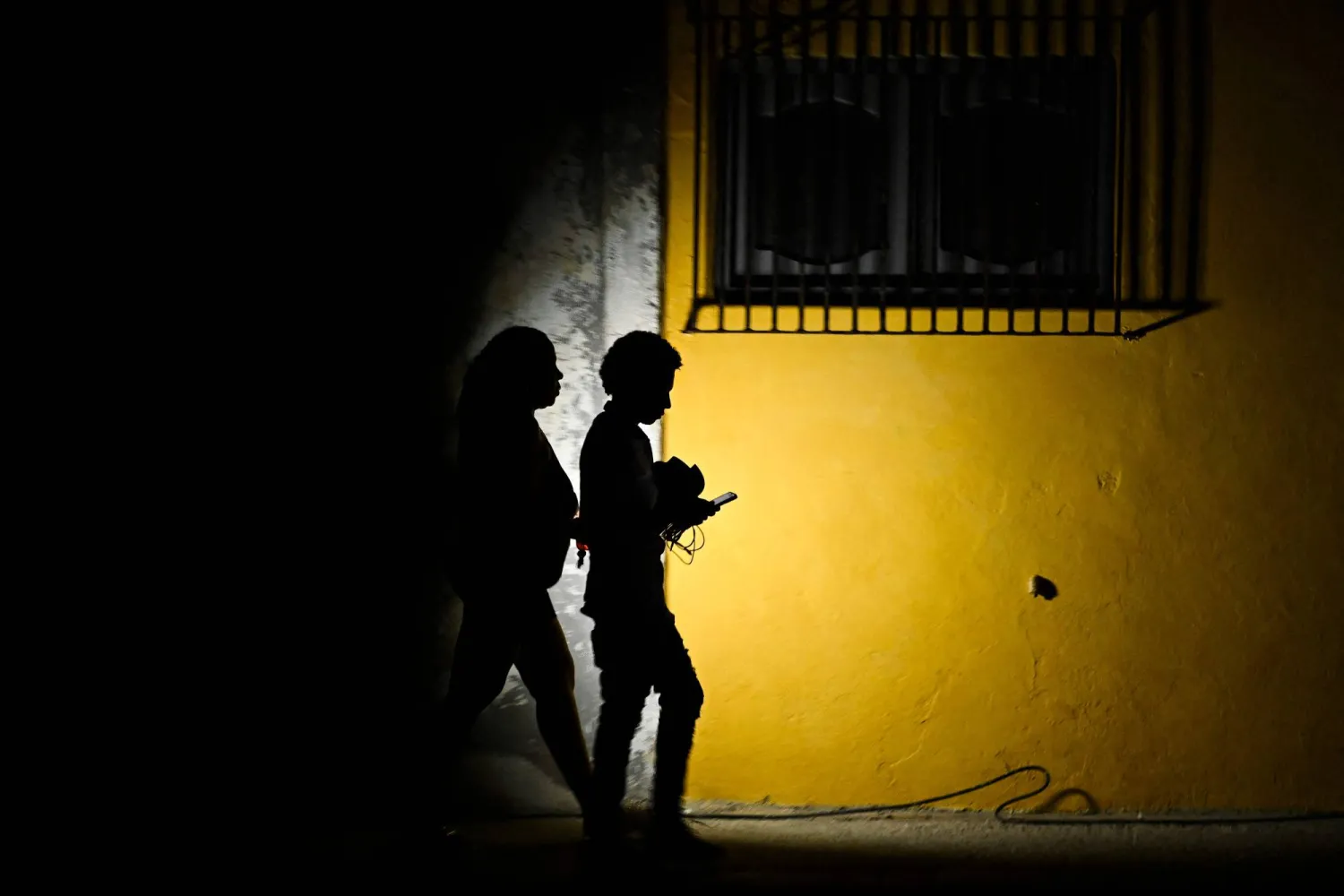 A woman holds a flashlight while walking with a man on a street during a blackout in Havana on March 16, 2026. (AFP)