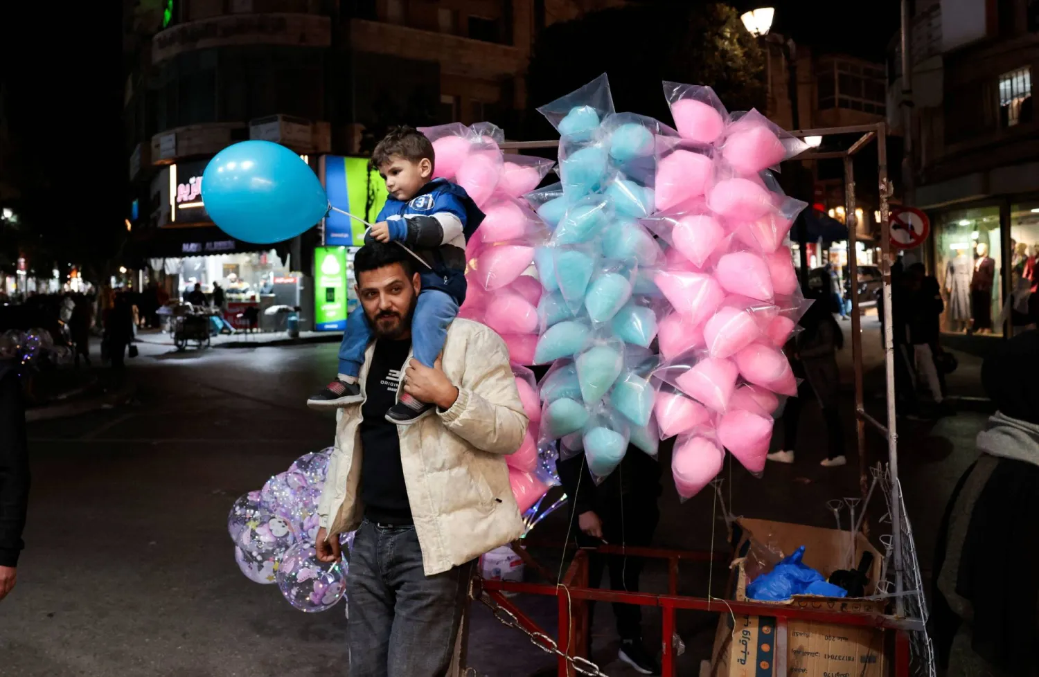 فلسطيني يحمل ابنه يوم الثلاثاء في رام الله بالضفة الغربية قبل حلول عيد الفطر  (رويترز)