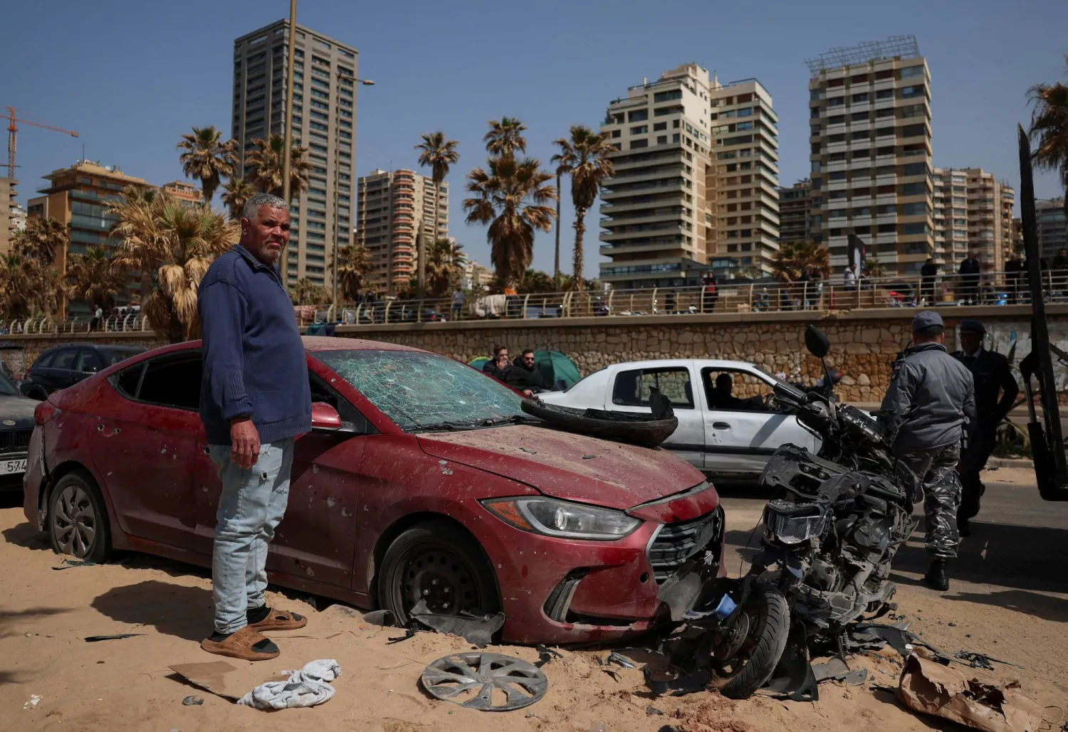 A man stands by a damaged car, at the site of a drone strike targeting a car in Ramlet al-Baida at Corniche Beirut, following an escalation between Hezbollah and Israel amid the US-Israeli conflict with Iran, in Beirut, Lebanon, March 12, 2026. REUTERS/Claudia Greco   