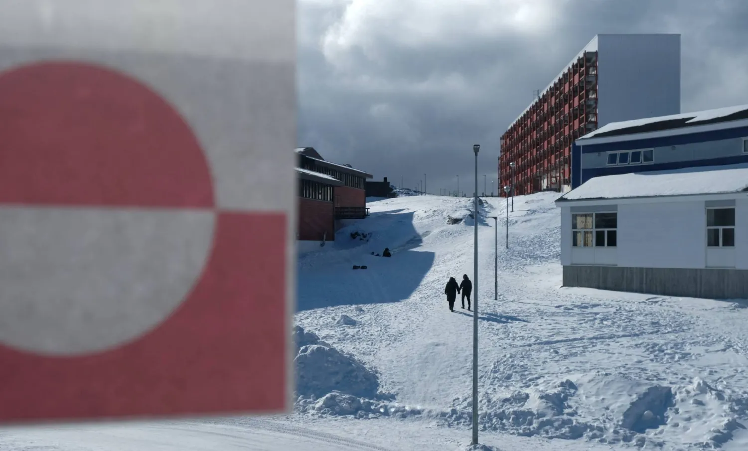 أشخاص يسيرون بجوار علم غرينلاند في نوك (رويترز)