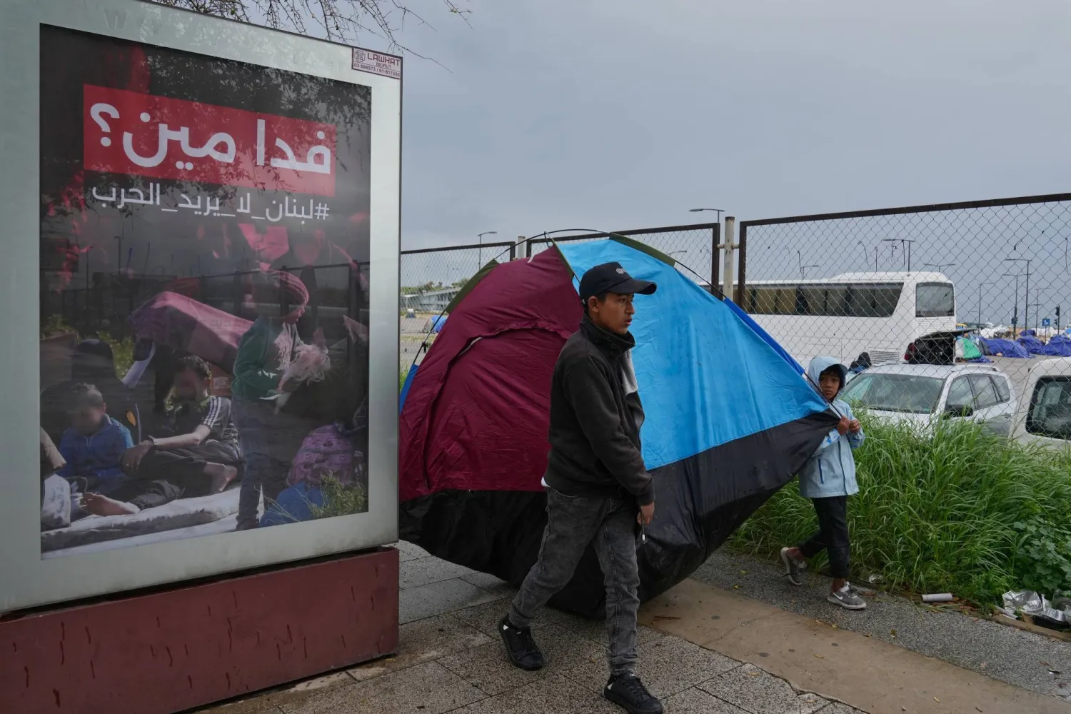 نازح من جنوب لبنان إلى وسط بيروت وإلى جانبه لوحة إعلامية تتضمن شعاراً مناهضاً للحرب (أ.ب)