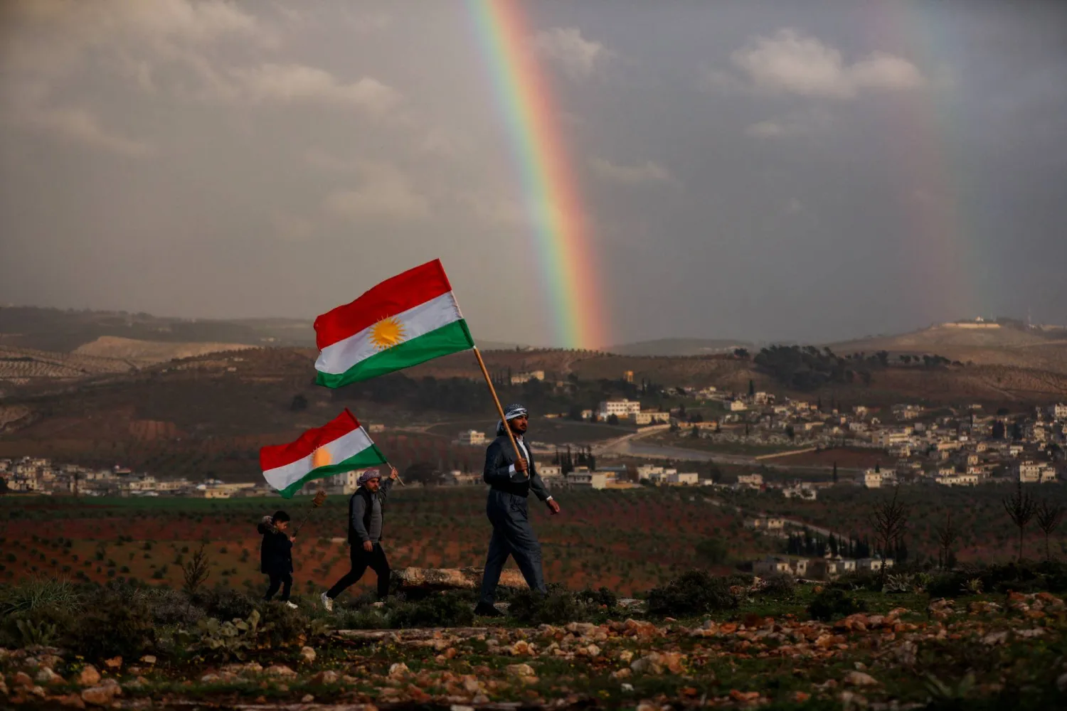 سوريون أكراد يحملون أعلاماً كردية استعداداً للاحتفال بـ«النوروز» في عفرين بمدينة حلب الجمعة (رويترز)