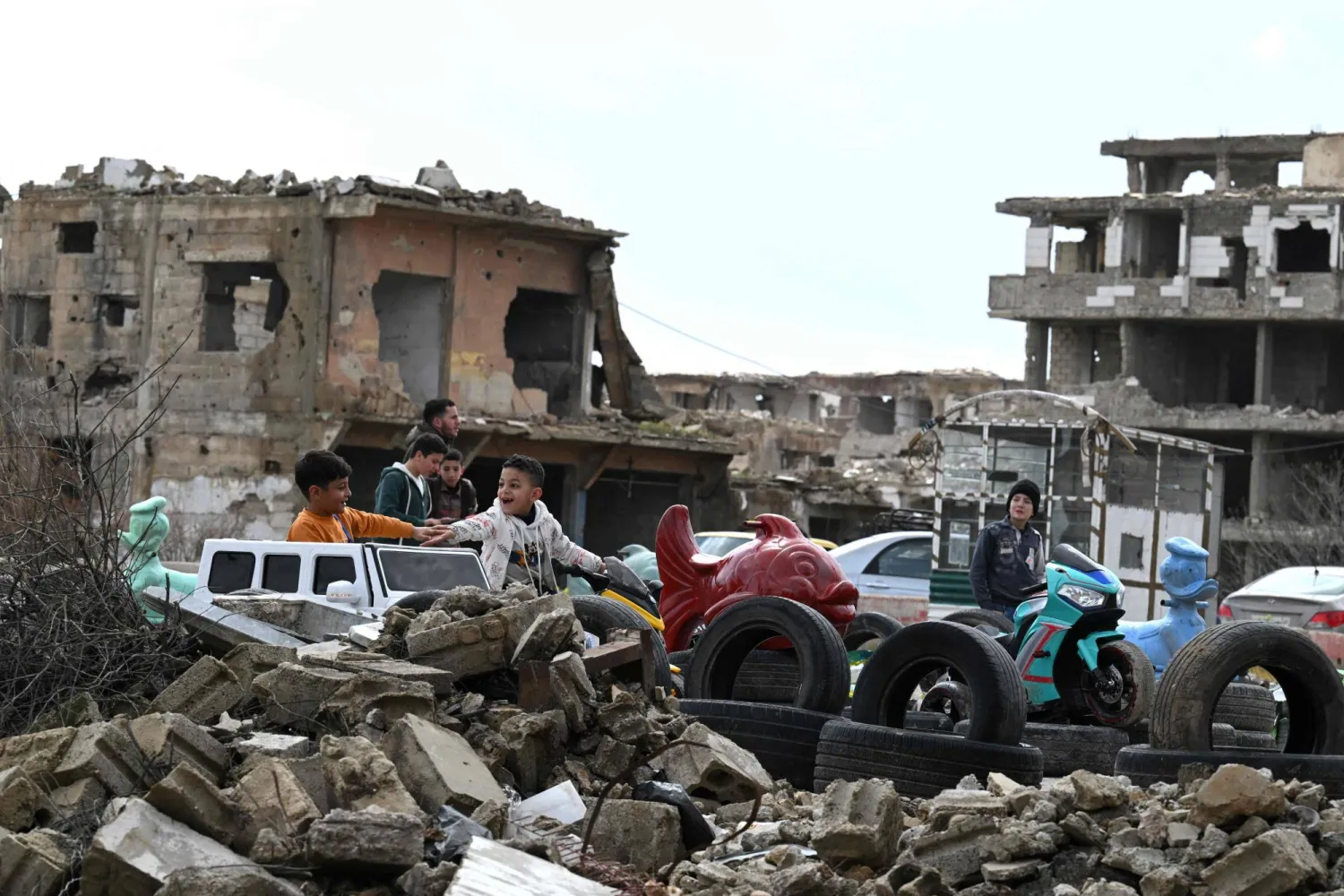  أطفال سوريون في مدينة ملاهٍ أُقيمت على أرض محاطة بمبانٍ مدمرة في حي جوبر بدمشق الأحد (أ.ف.ب)