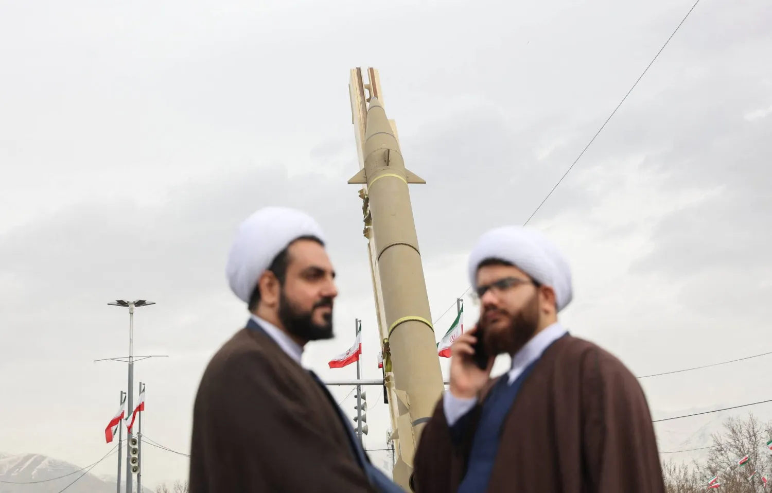 رجلا دين يشاركان في مراسم إحياء ذكرى الثورة فيما يُعرض صاروخ باليستي بميدان آزادي غرب طهران (رويترز)