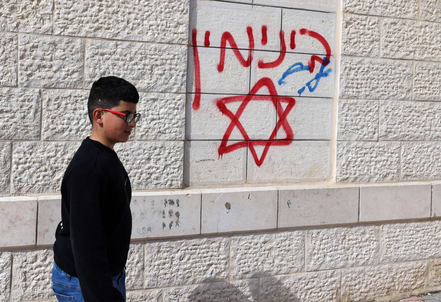 طفل فلسطيني يمرّ يوم الأحد بجوار كتابات عبرية مسيئة على جدران منزل متضرر من هجوم المستوطنين في قرية جلود جنوب نابلس بالضفة الغربية (أ.ف.ب)