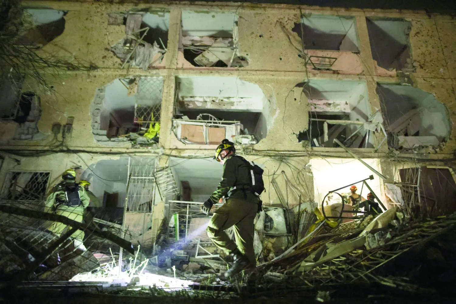 جندي إسرائيلي يستخدم مصباحاً يدوياً لتفقد الأضرار التي خلفها صاروخ إيراني في ديمونة (رويترز) 