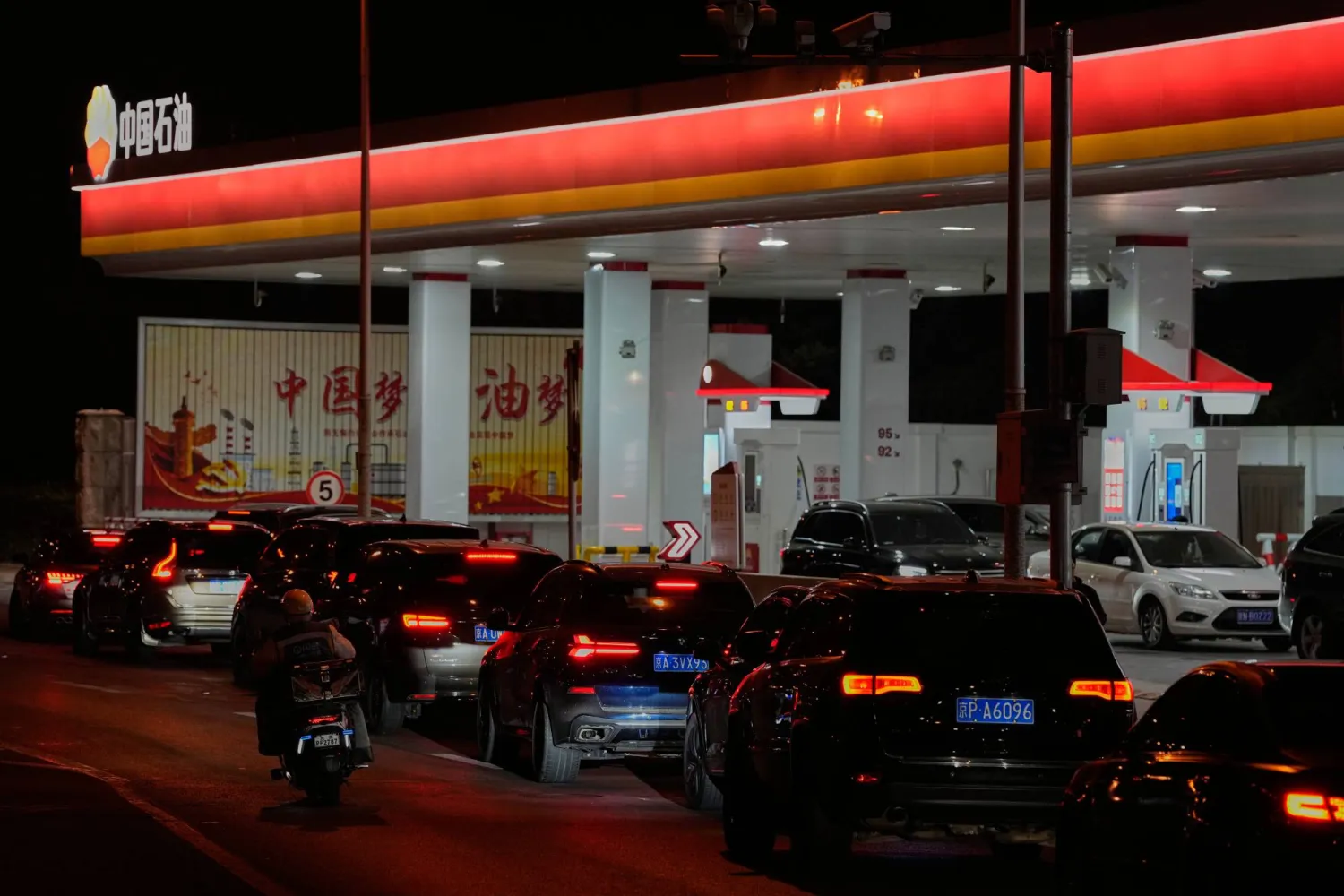 A rider passes by motorists queue to pump gasoline at a petrol station in Beijing, Sunday, March 22, 2026. (AP Photo/Andy Wong)