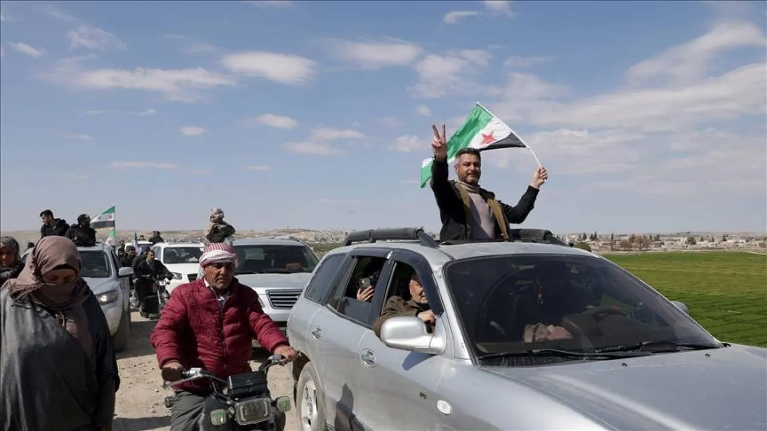 رفع العلم السوري مع عودة أهالي ناحية الشيوخ في عين العرب بريف حلب إلى منازلهم وبعضهم على الدراجات أو على الأقدام (أناضول)