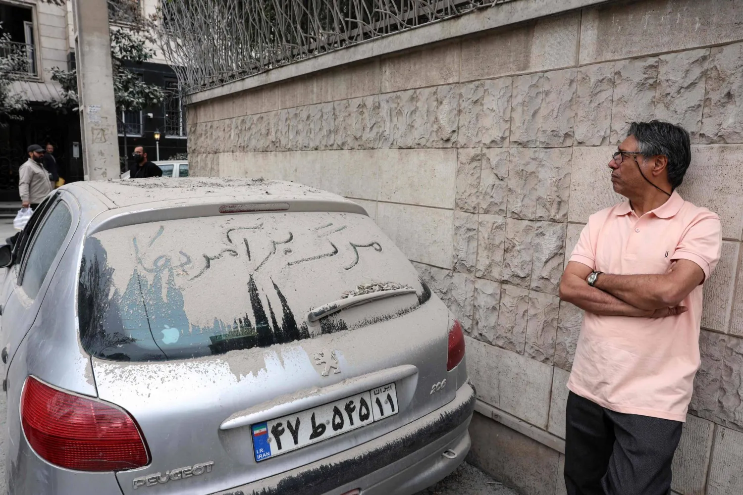 A resident looks at the damage to a destroyed apartment block in northern Tehran as he stands next to a dust-covered car with the words "Down with the USA" written on its rear window on March 23, 2026. (AFP)